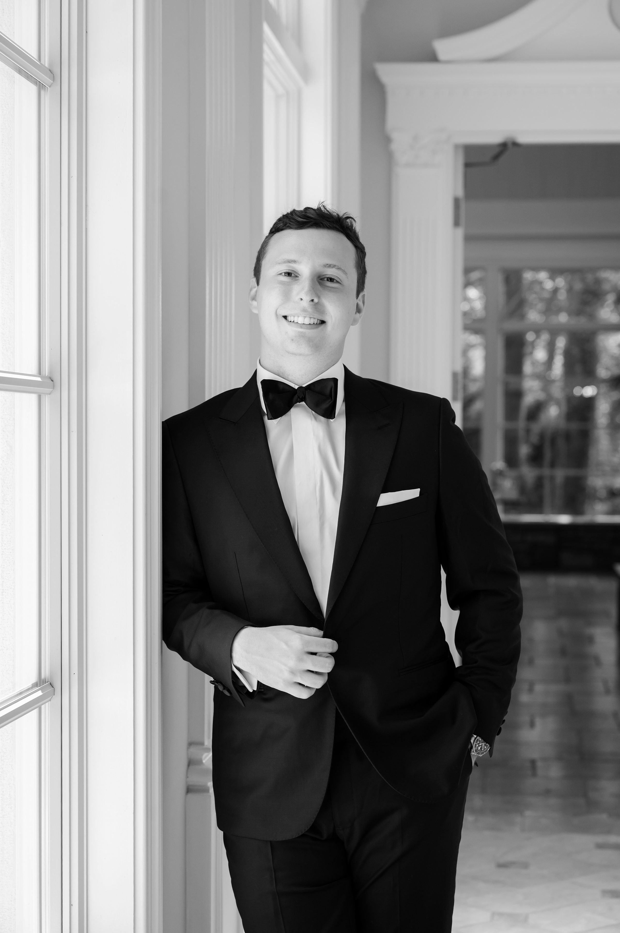 Black and white portrait of the groom leaning against the wall, looking at the camera