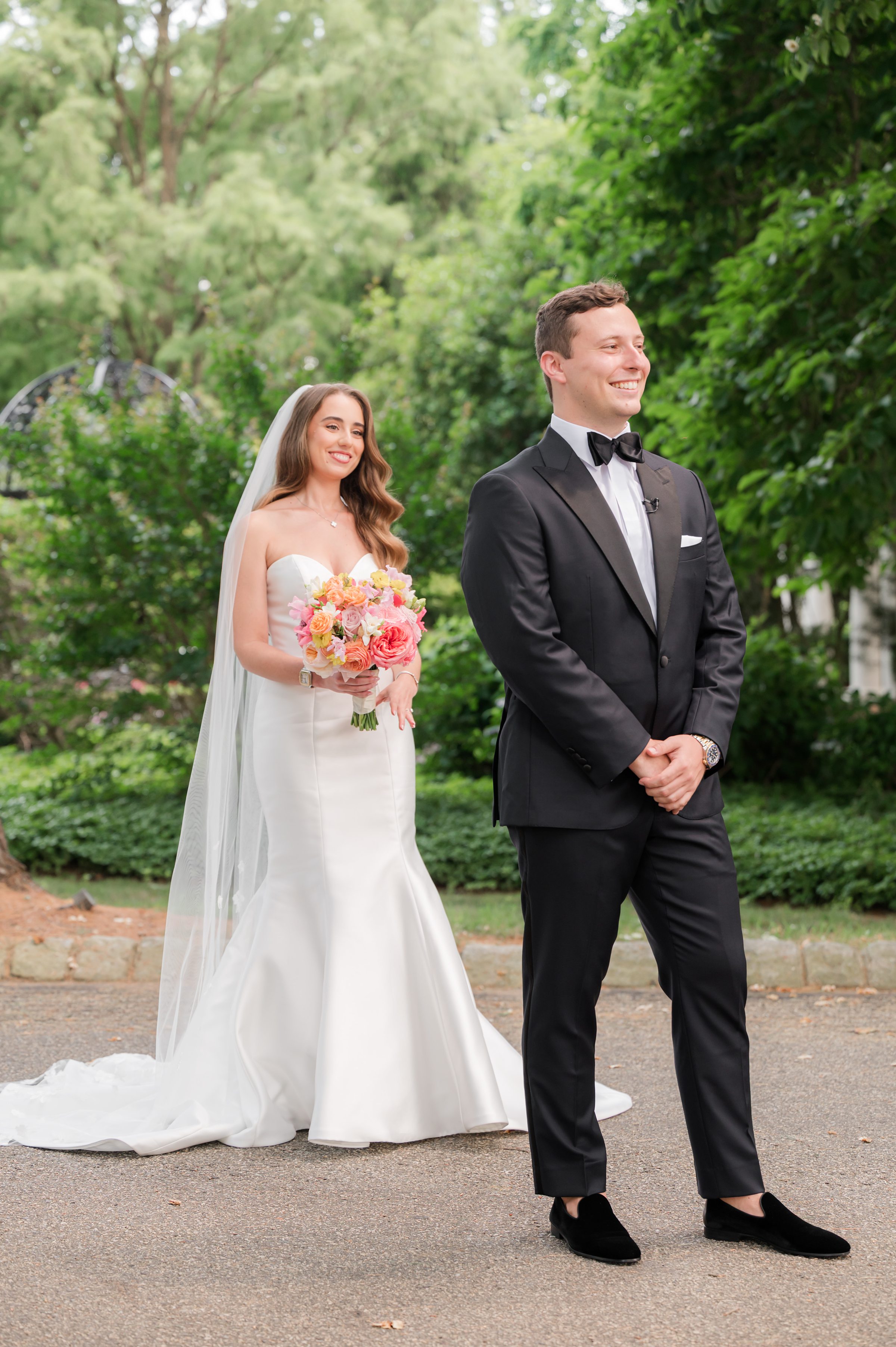Bride holding a summer palette bouquet standing behind the groom for the first look