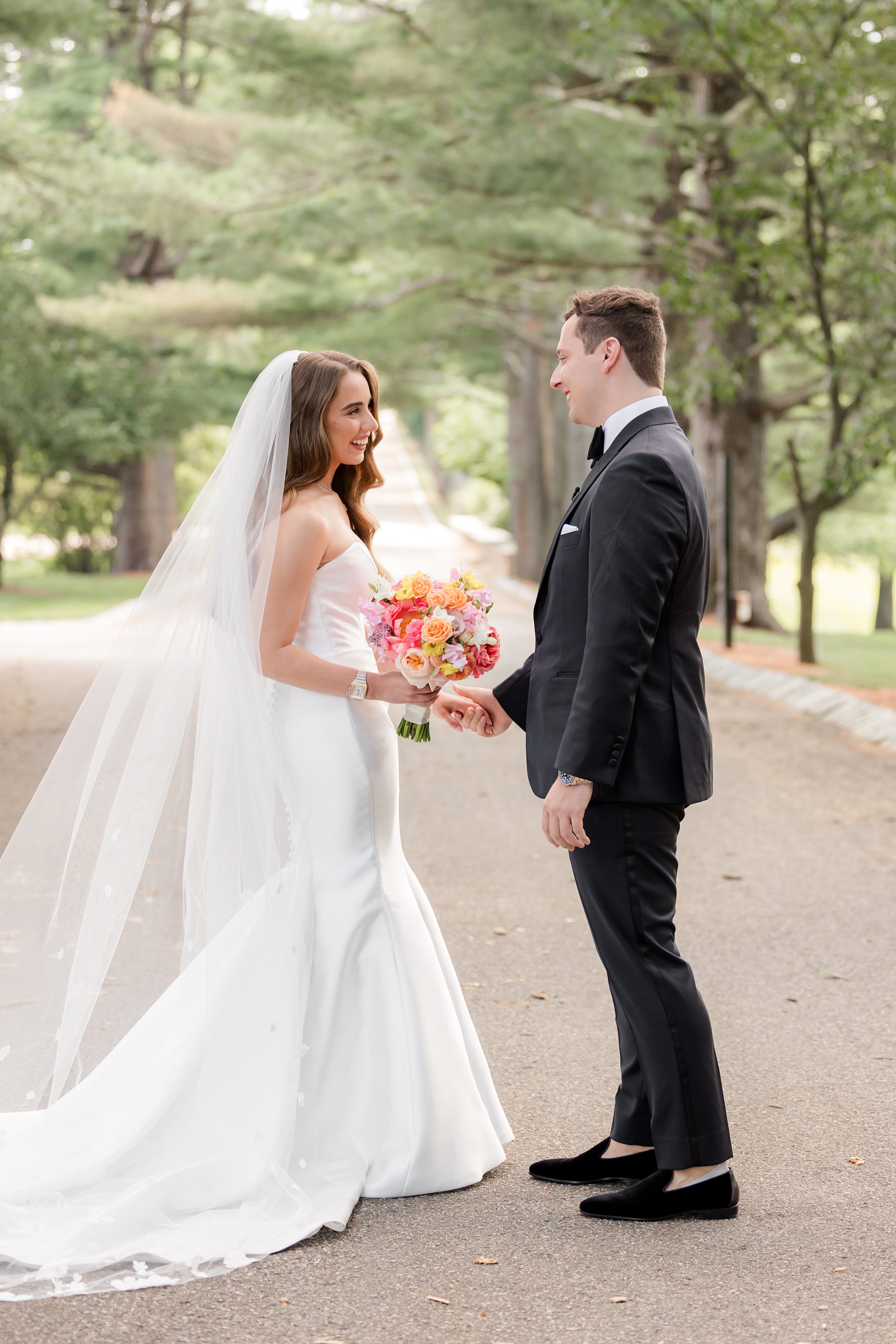 Full-body portrait of groom and bride looking at each other with trees as the background