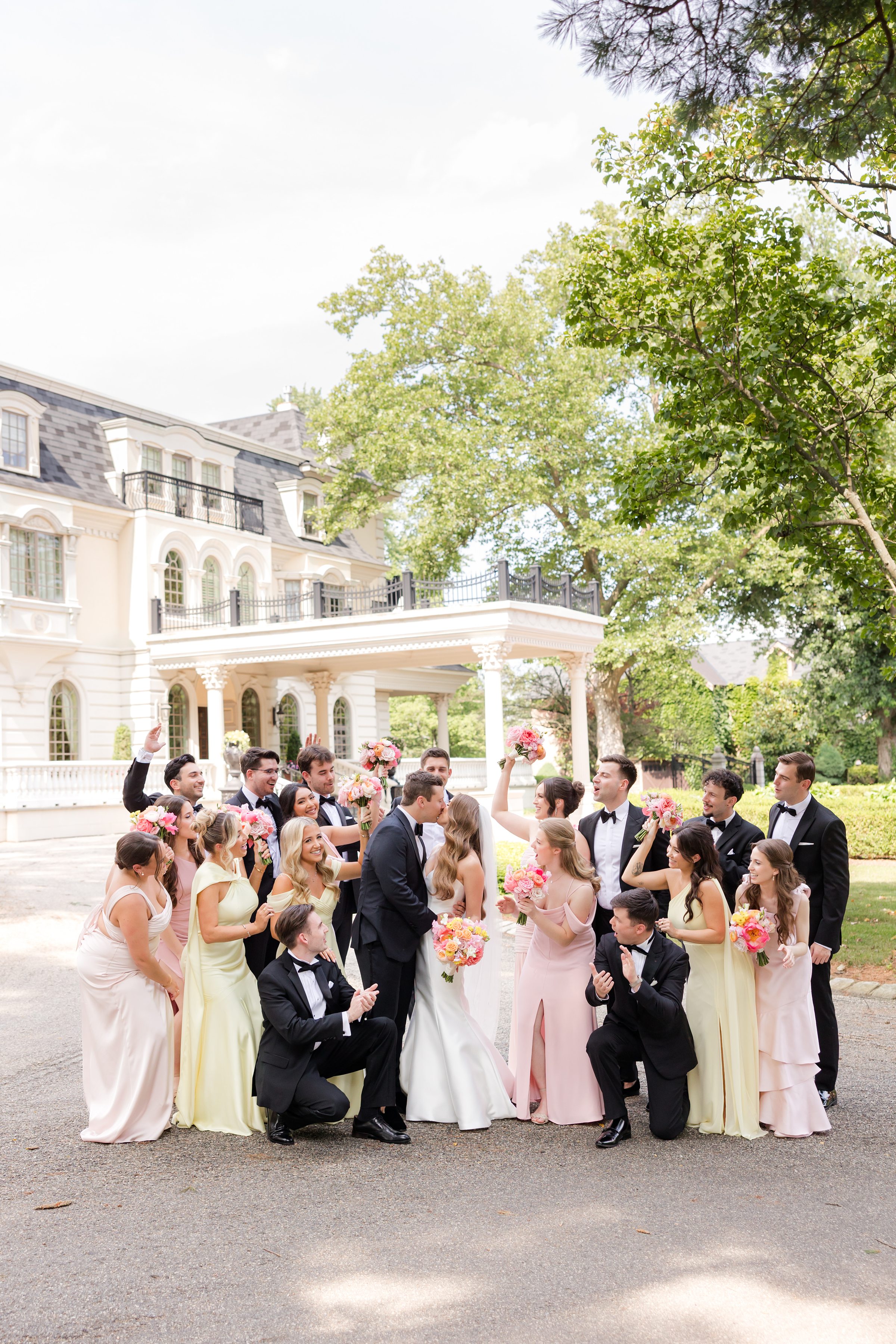 Portrait of wedding party surrounding and cheering on the bride and groom as they go for a kiss
