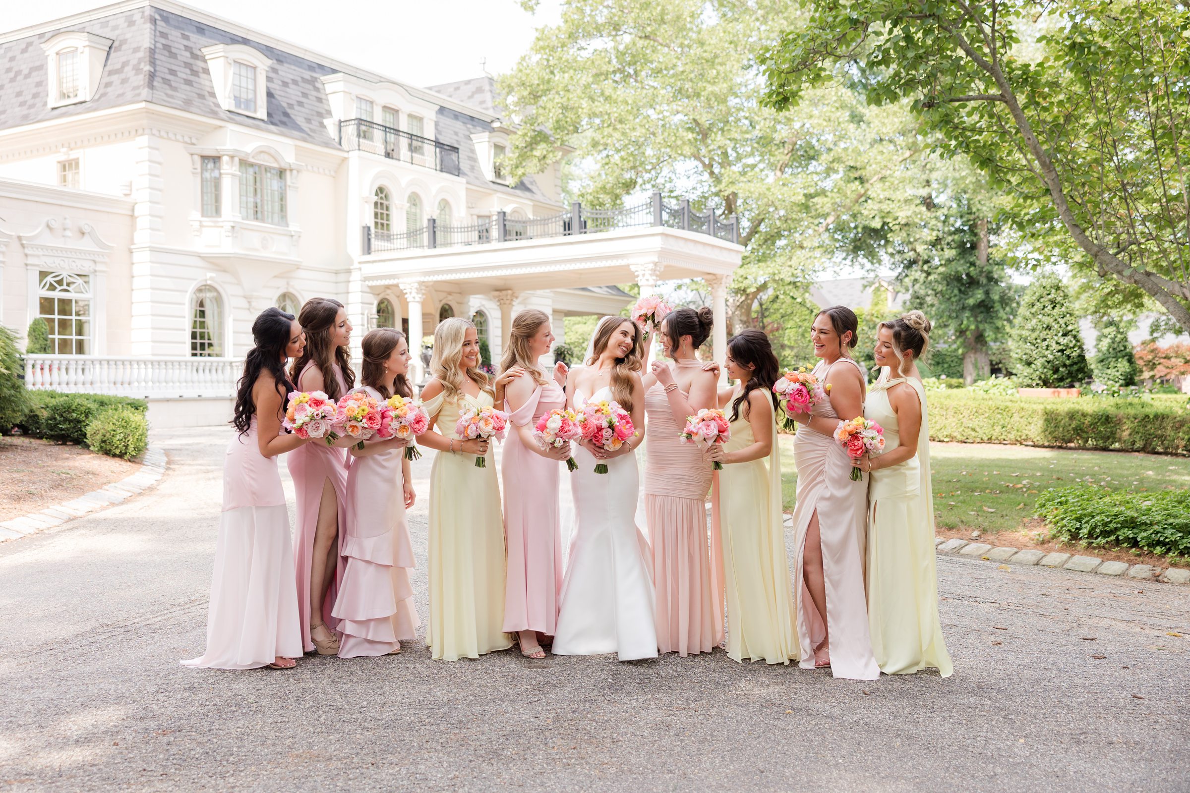 Bride looking at her bridesmaids while they all stand beside each other holding their pink, white, and yellow bouquet