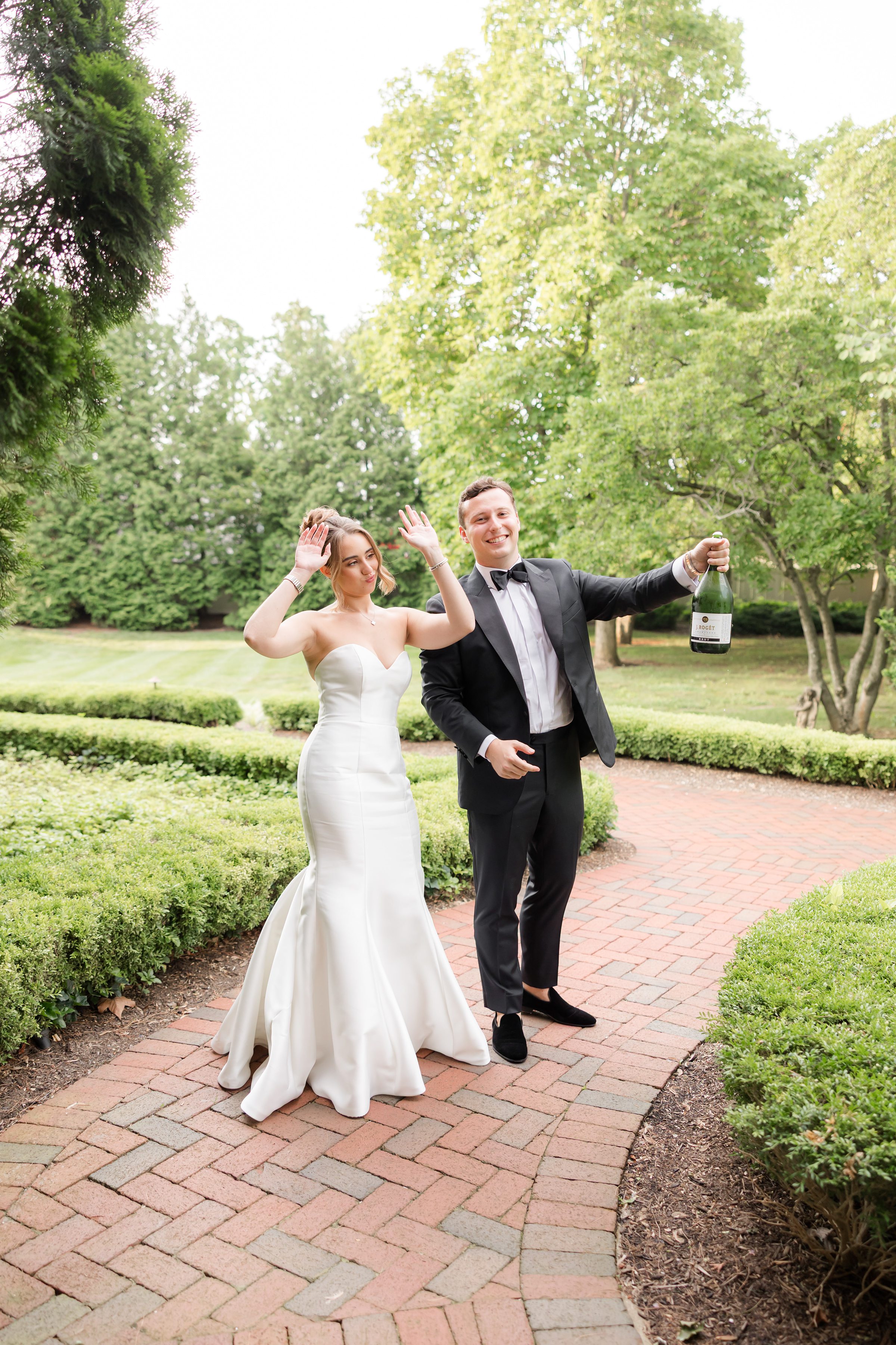 Bride and groom posing, the bride is holding her hands up and the groom is holding one bottle of champagne. 