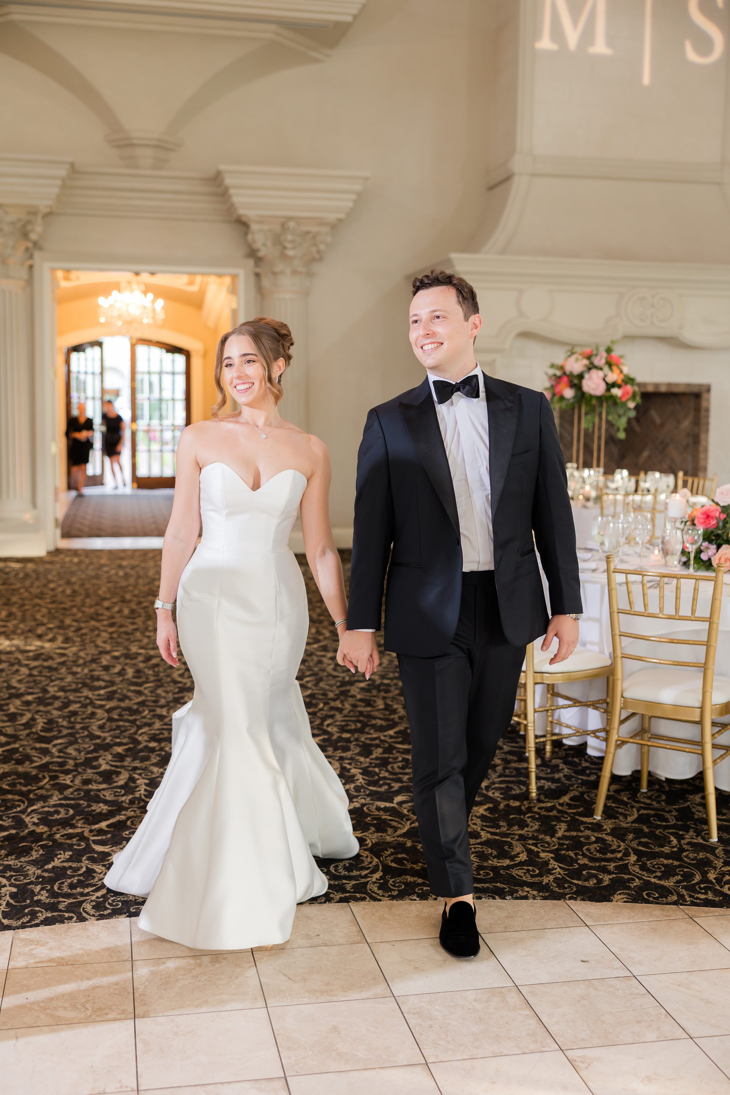 Bride and groom in the reception hall, smiling while holding hands together