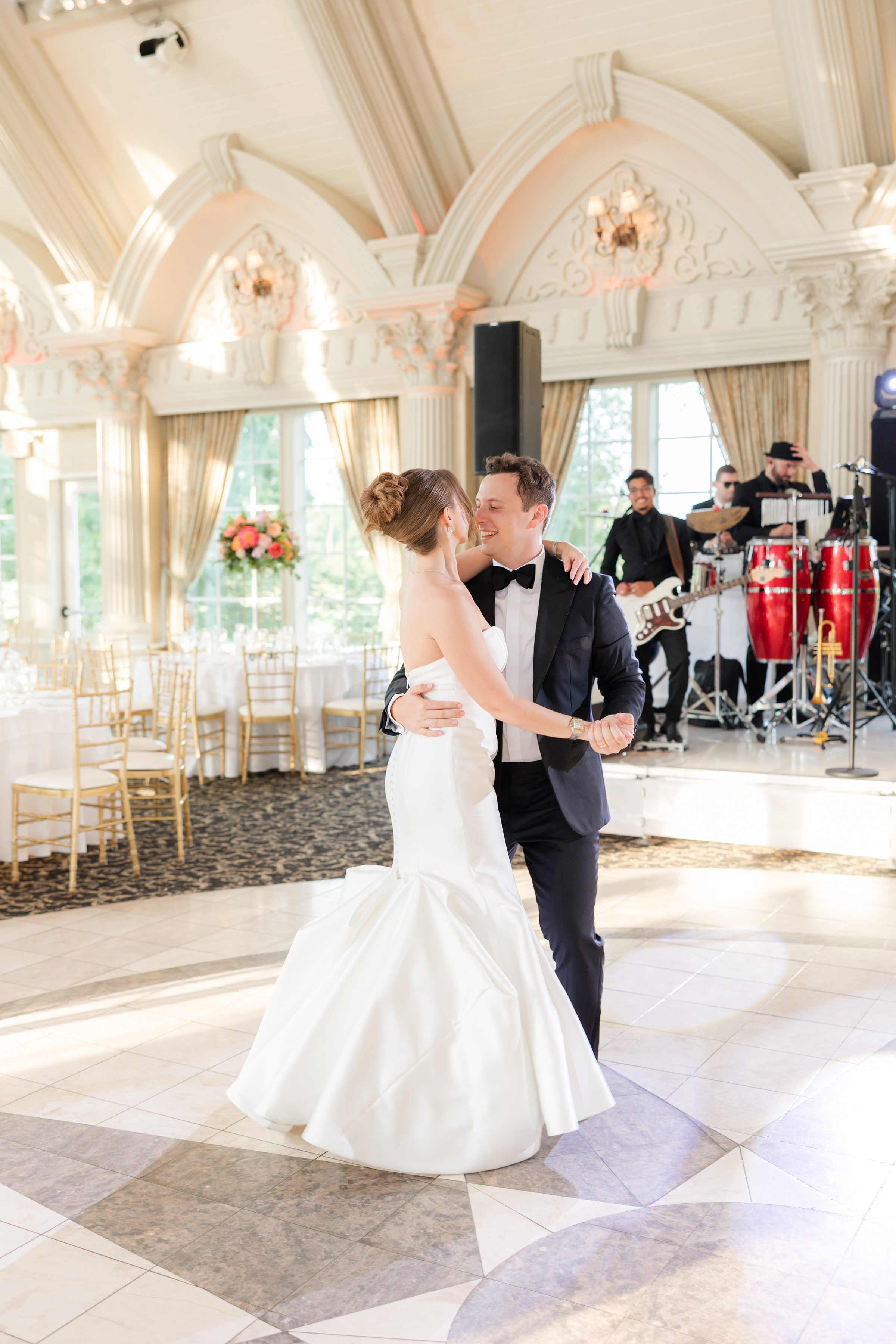 Bride and groom dancing, Groom is smiling at the bride with the music band in the background