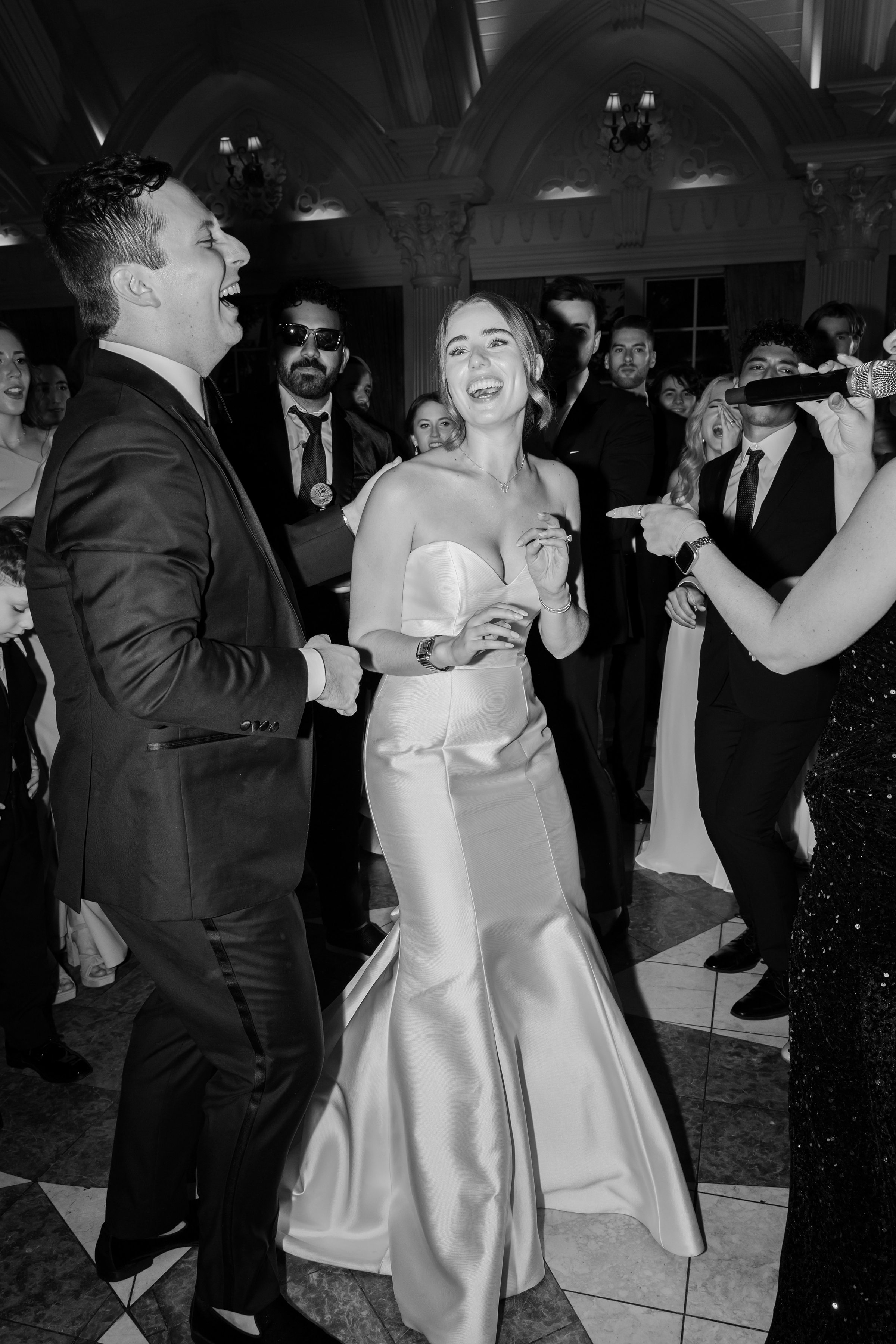 Bride and groom laughing while dancing with guests, picture is in black and white