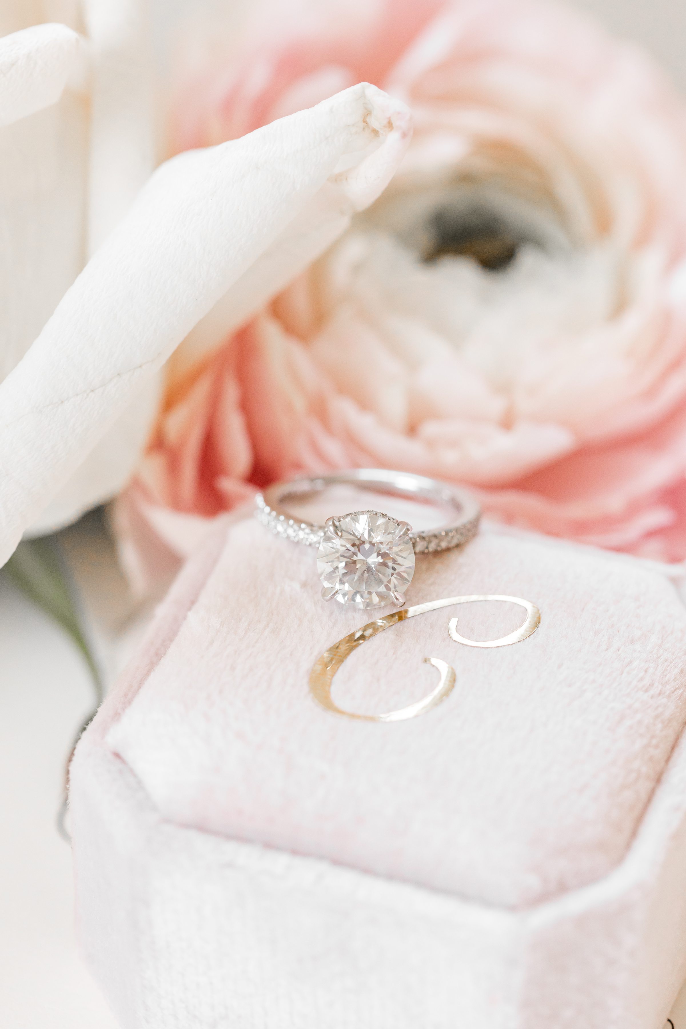 a close-up picture of bride's diamond ring placed on the ring box with pink flowers in the back