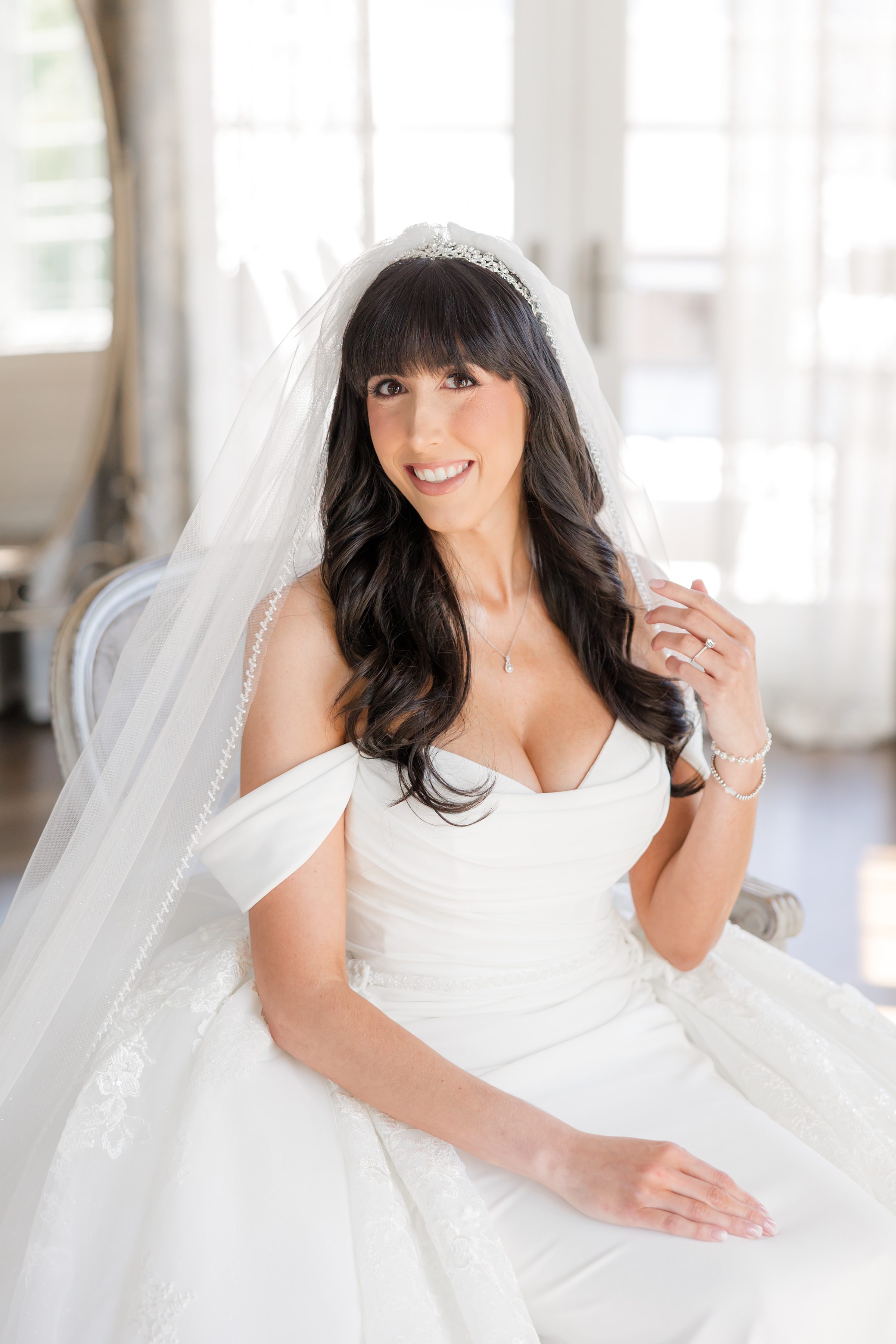 a portrait picture of bride sitting, wearing her off-shoulder wedding dress, smiling at the camera