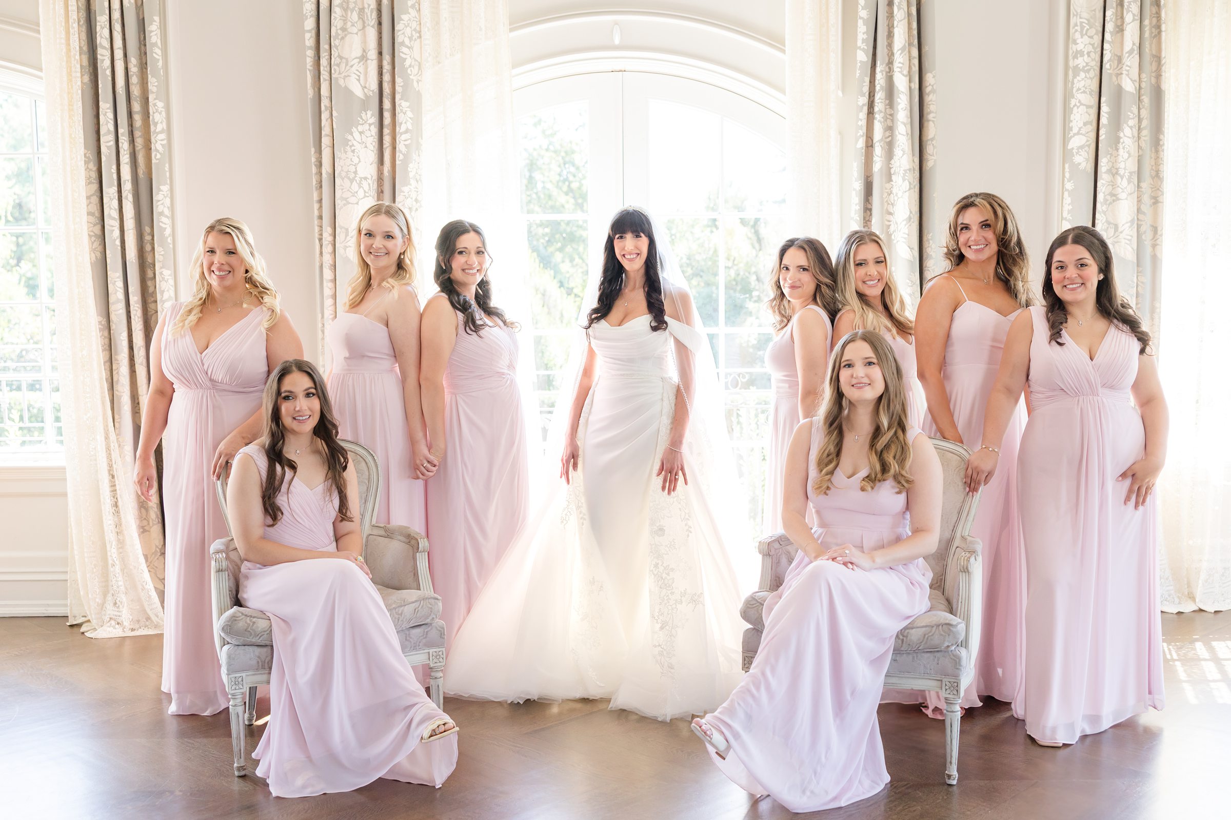 bride posing with bridesmaids by the window wearing soft pink palette and two of the bridesmaids are sitting in front