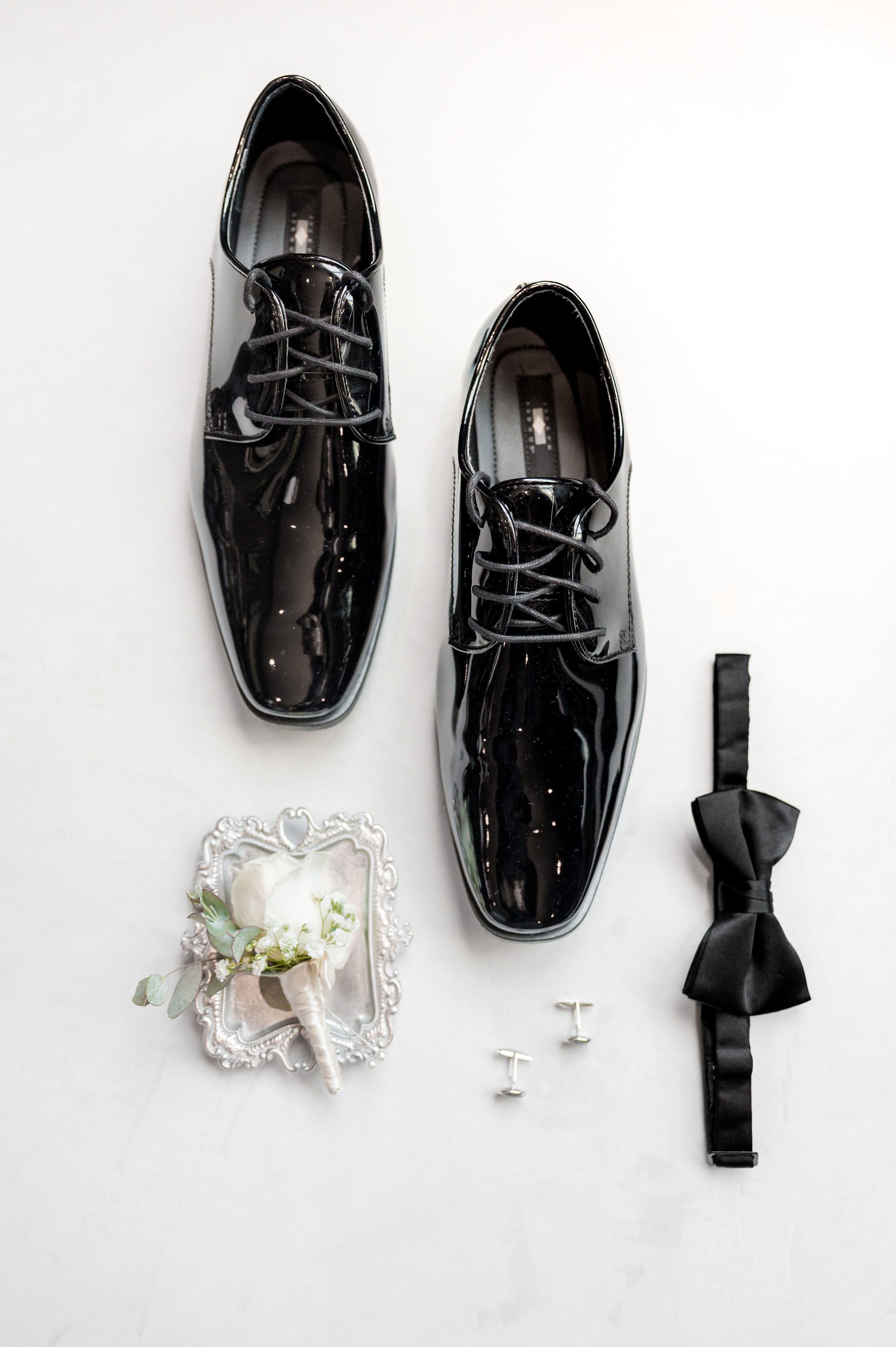 a detail shot of groom's wedding shoes with bowtie, cufflinks and cream flower