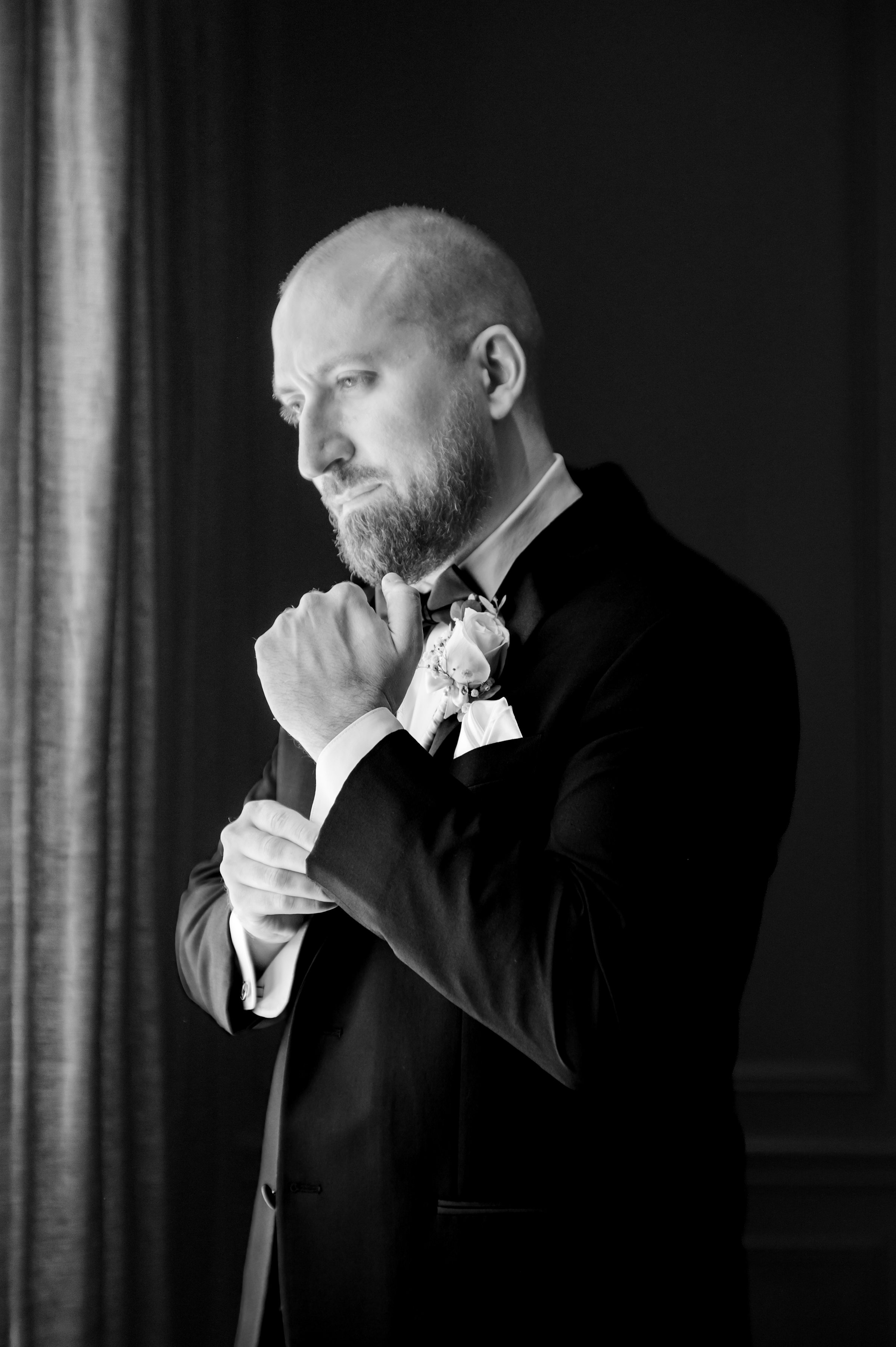 a portrait picture of groom looking down to the side while fixing his cuffs, picture in black and white