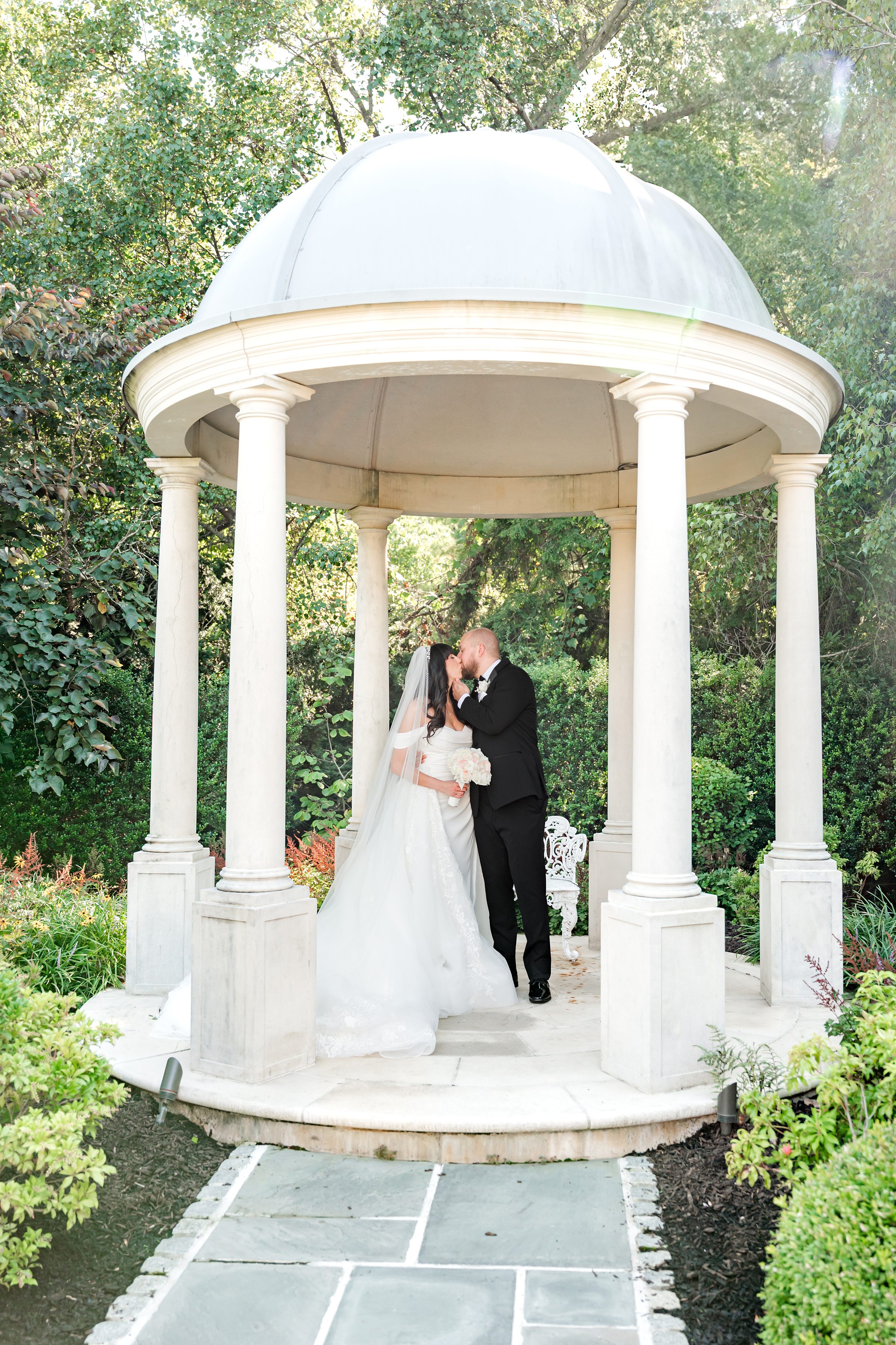 Bride and groom kissing in the gazebo, while the groom is holding the bride's face