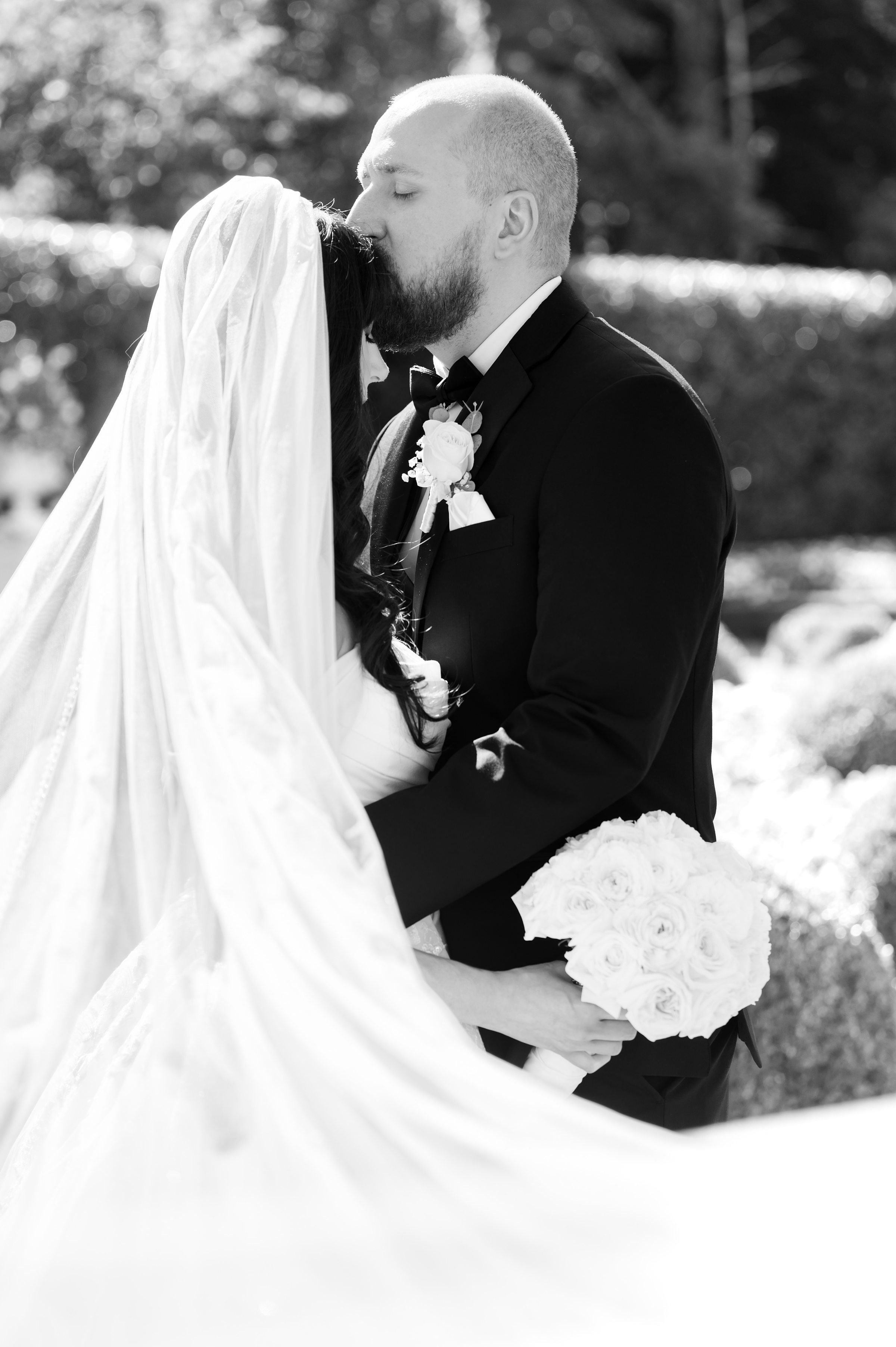 black and white portrait of groom kissing the bride's forehead