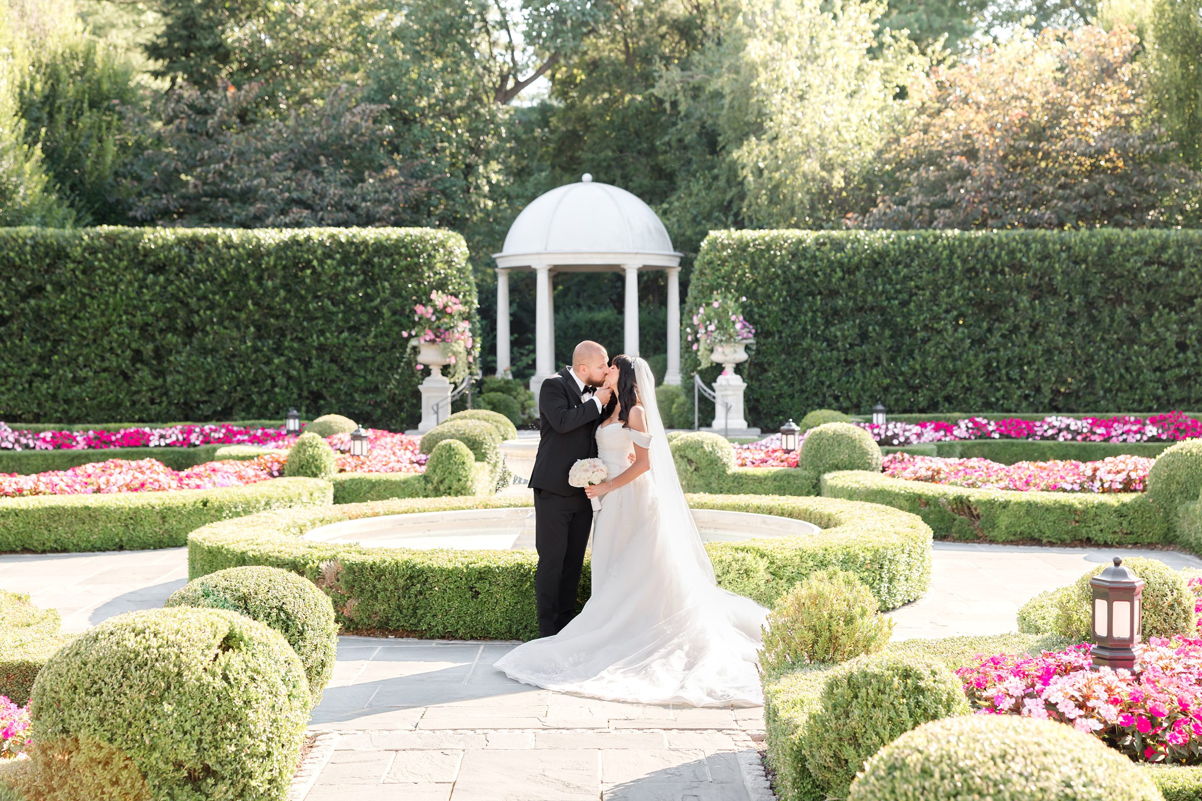 landscape picture of bride and groom kissing by the fountain with greenery 