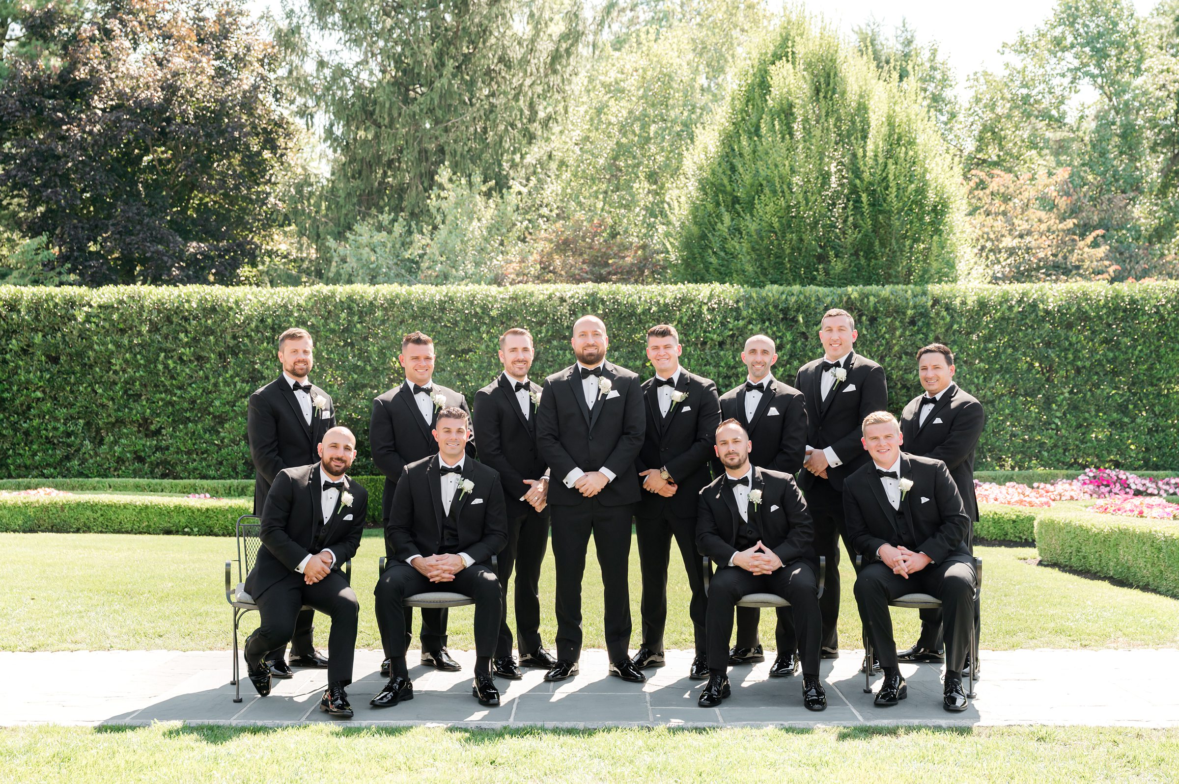 landscape photo of groom standing with groomsmen with 4 groomsmen sitting in front