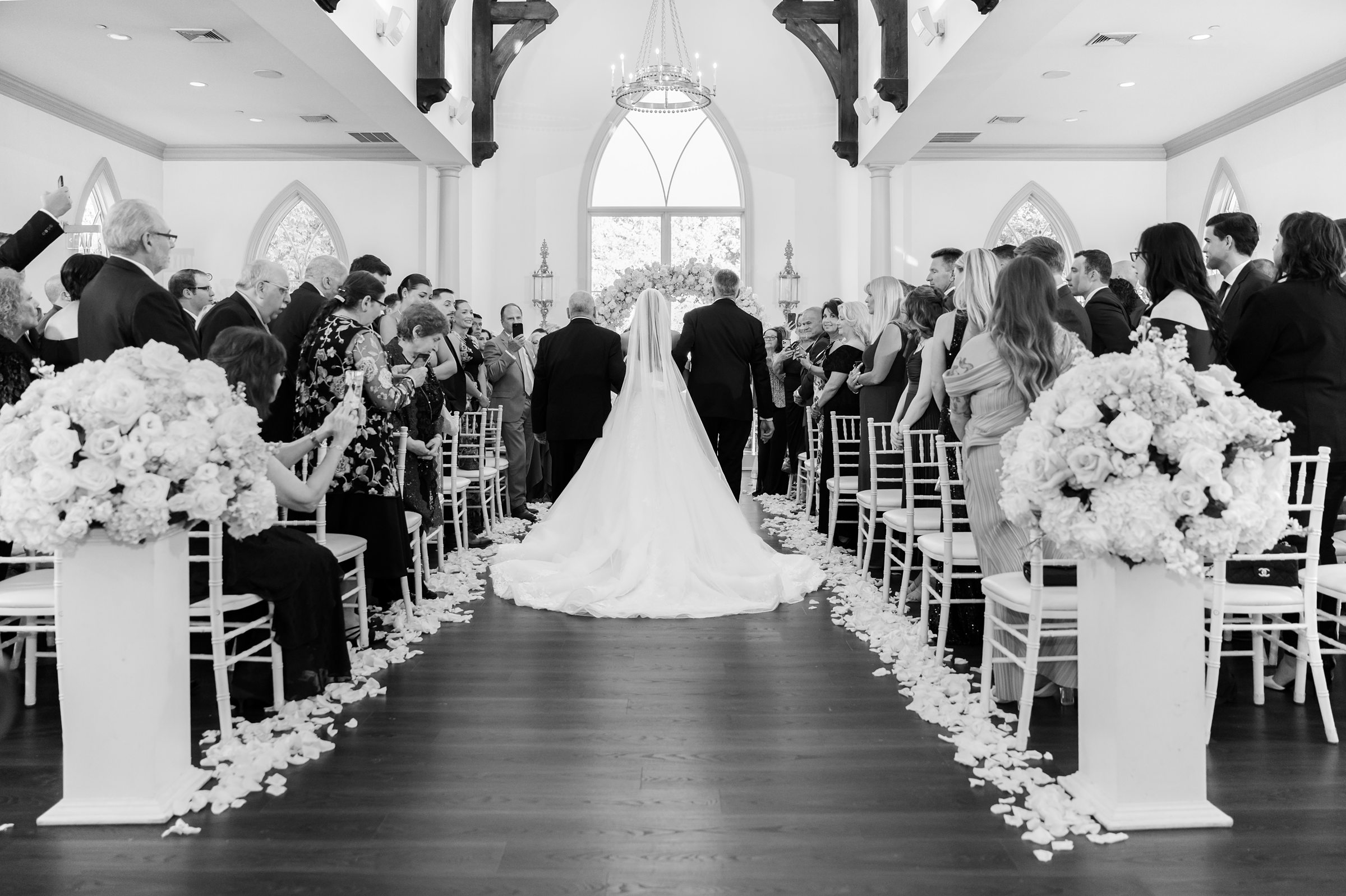 back shot of bride's relatives walk her down the aisle, picture in black and white