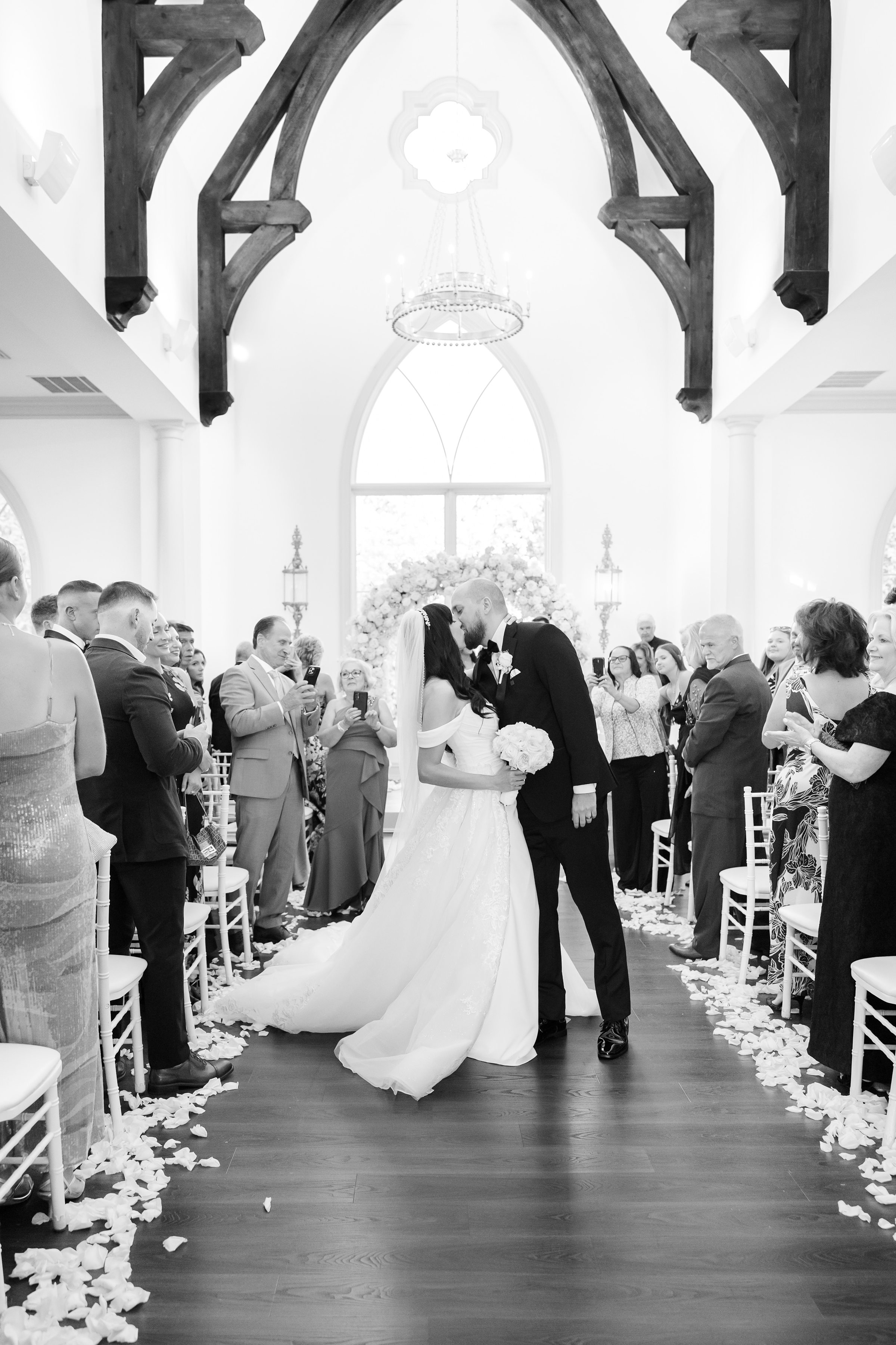 black and white photo of bride and groom kissing down the aisle