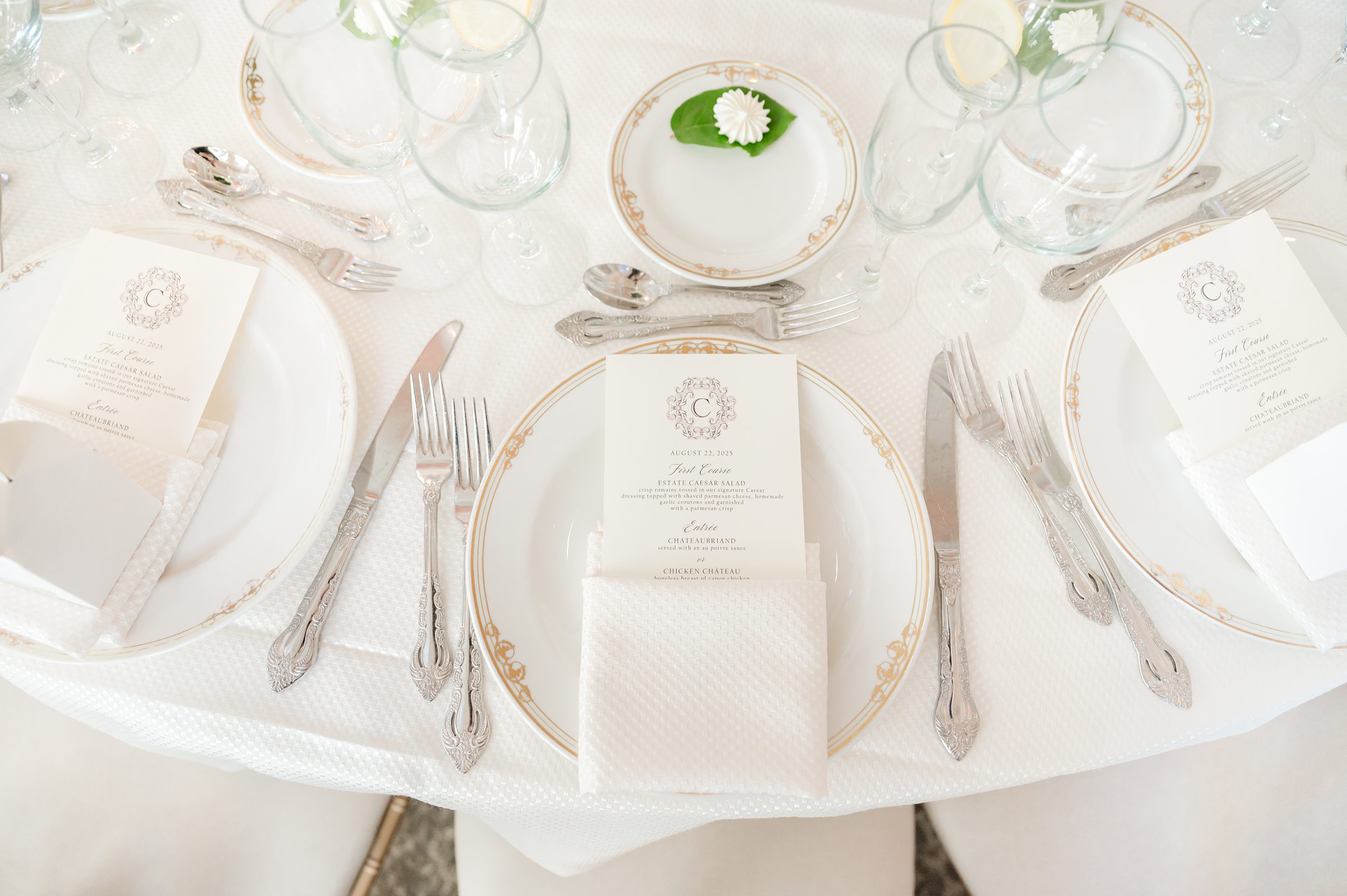 Detail shot of table setting with silver spoon and white plates with gold trims. On top of the plates are the menu cards wrapped in the table napkin