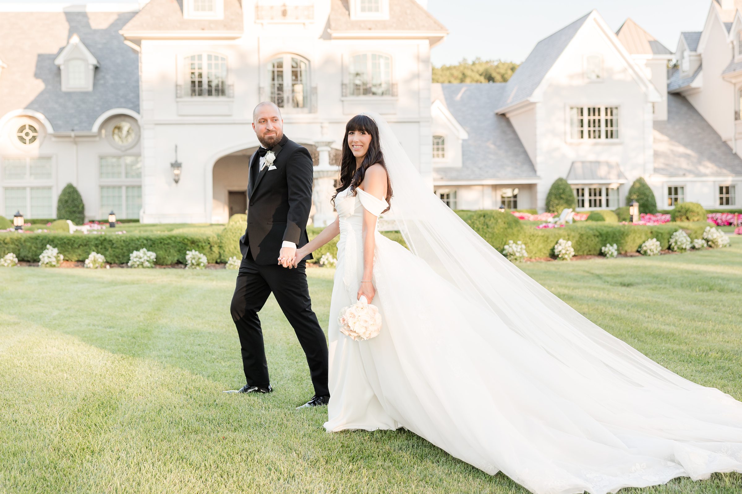Landscape photo of the bride and groom walking, while the groom is looking at the bride who is smiling at the camera