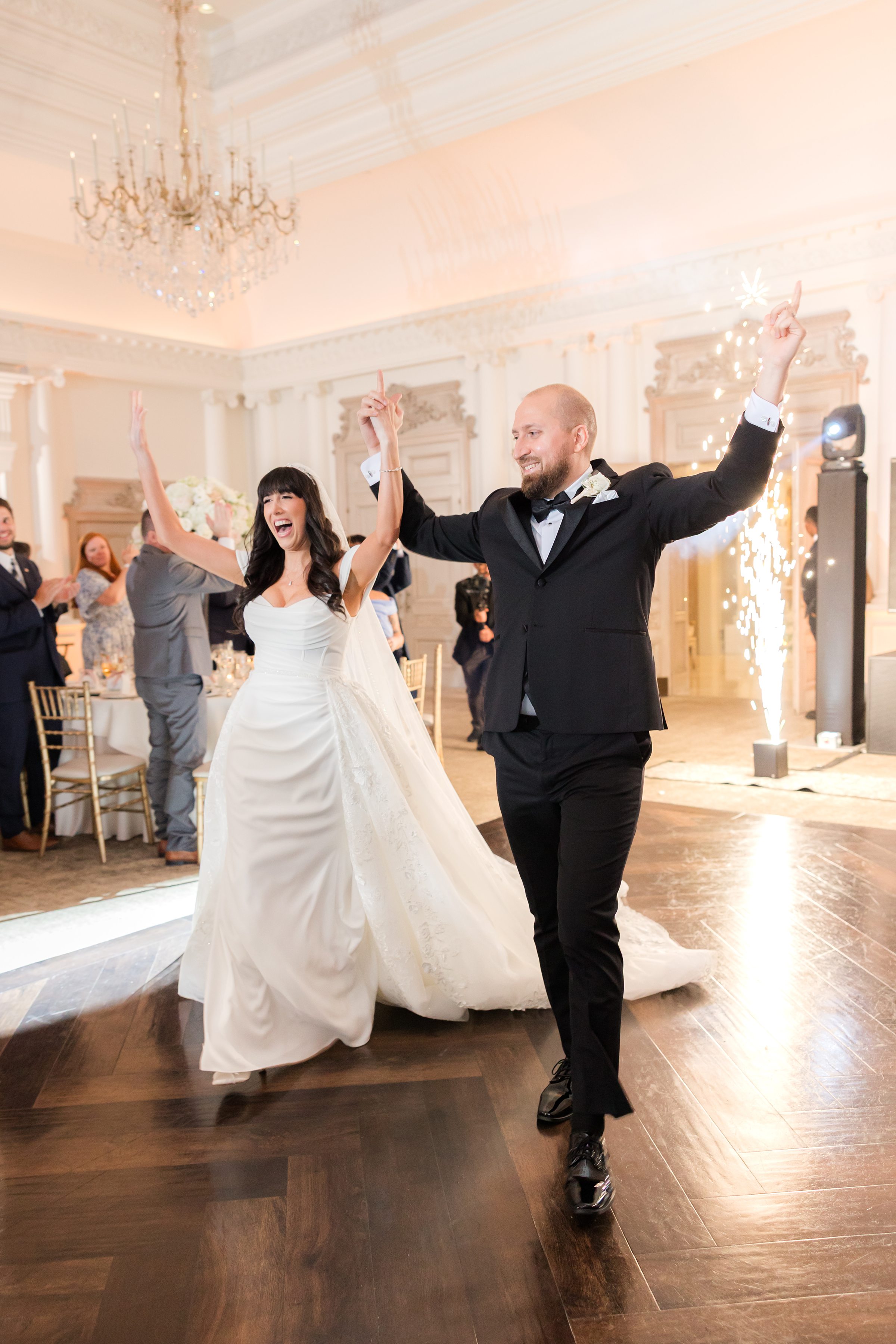 Bride and groom's grand entrance. Their hands are up in the air while they are joyfully celebrating, with spark fountains at the back