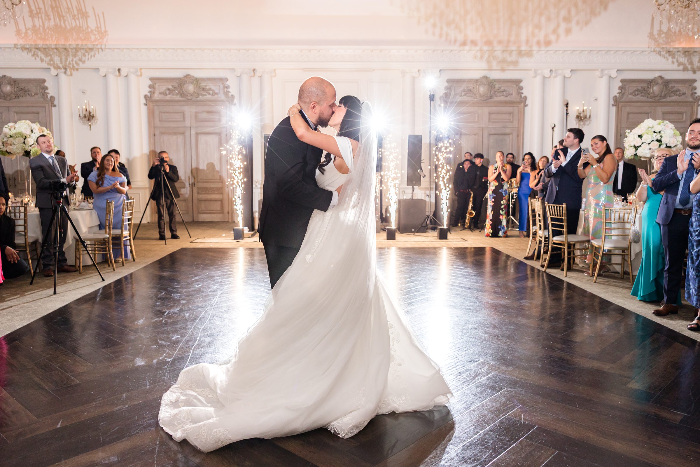 Bride and groom kissing on a wooden dancefloor with spark fountain and guests in the background