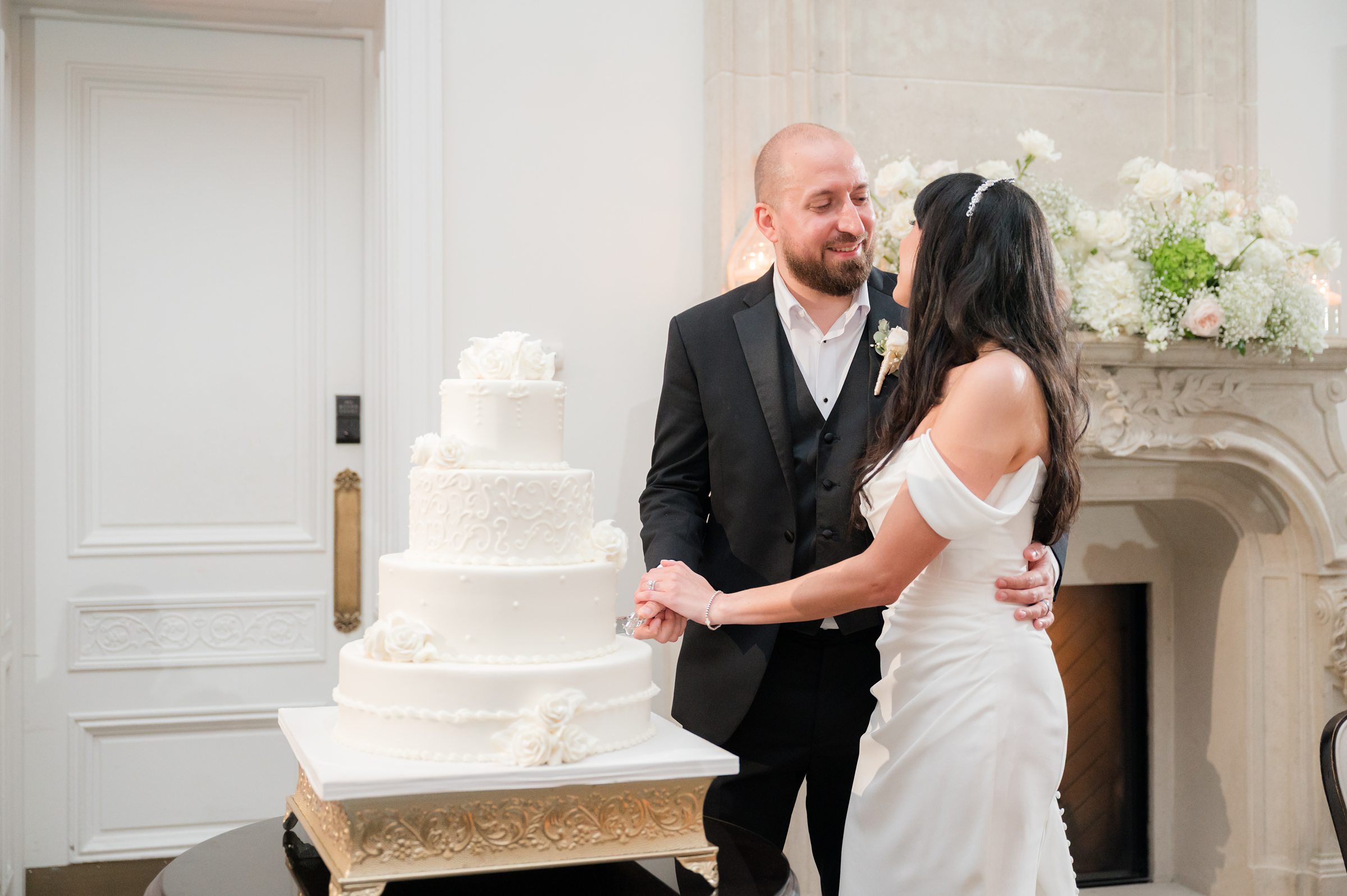 Landscape photo of the bride and groom looking at each other while they are both holding the knife for the cake cutting