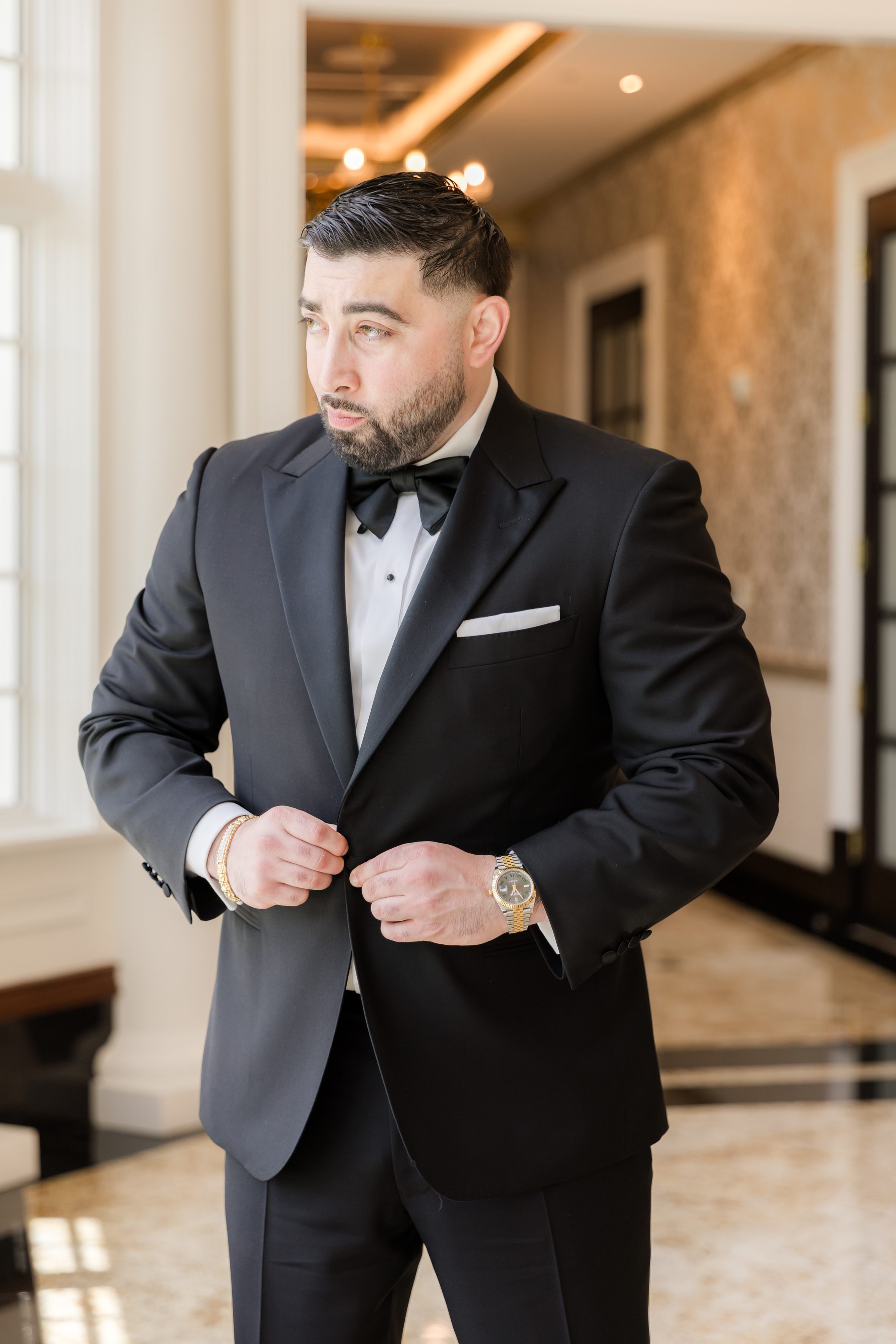 Portrait of groom looking out the window. Groom is wearing black tux with bow-tie, and has a beard and mustache