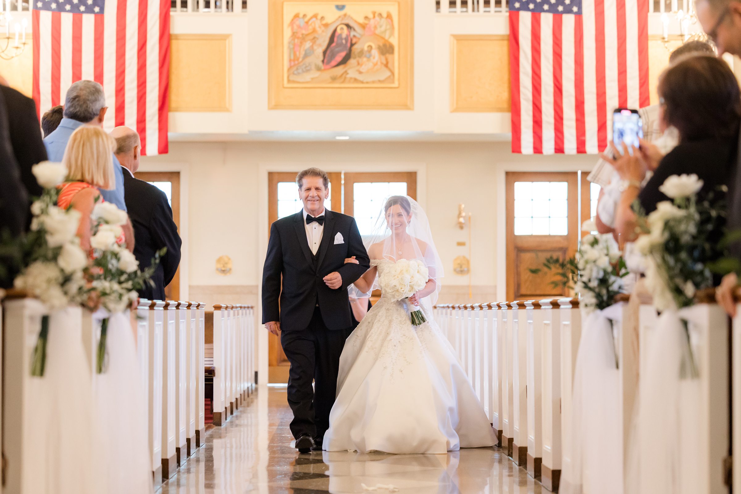Landscape photo of bride walking down the aisle with his father, while the guests are standing, looking at them