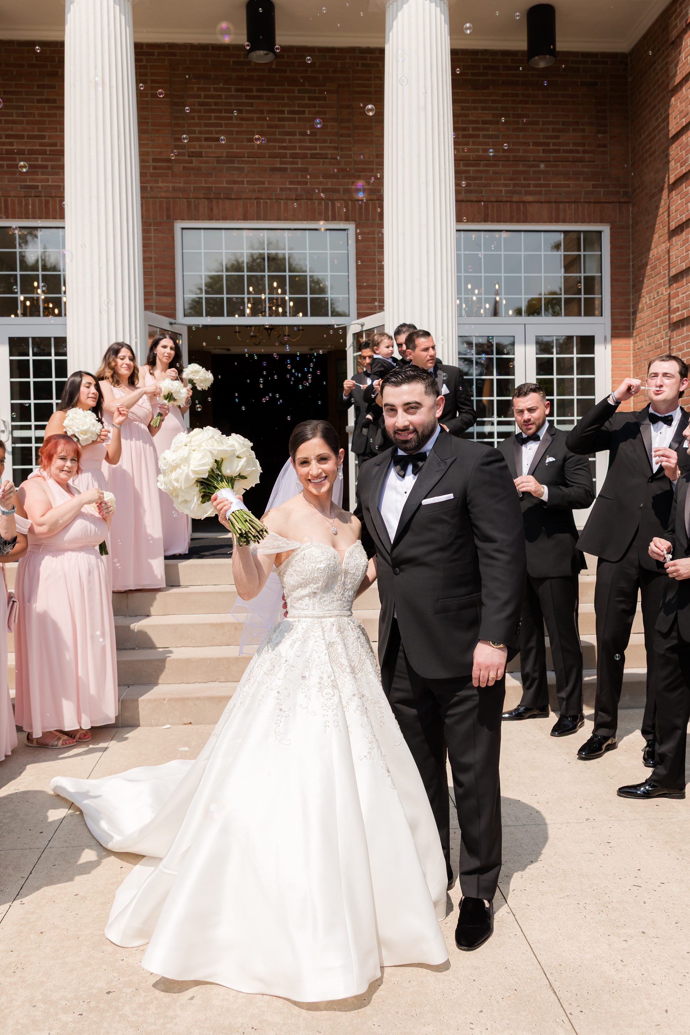Bride and groom at the entrance of the Church of Nativity, smiling at the camera with the wedding party lined up behind them