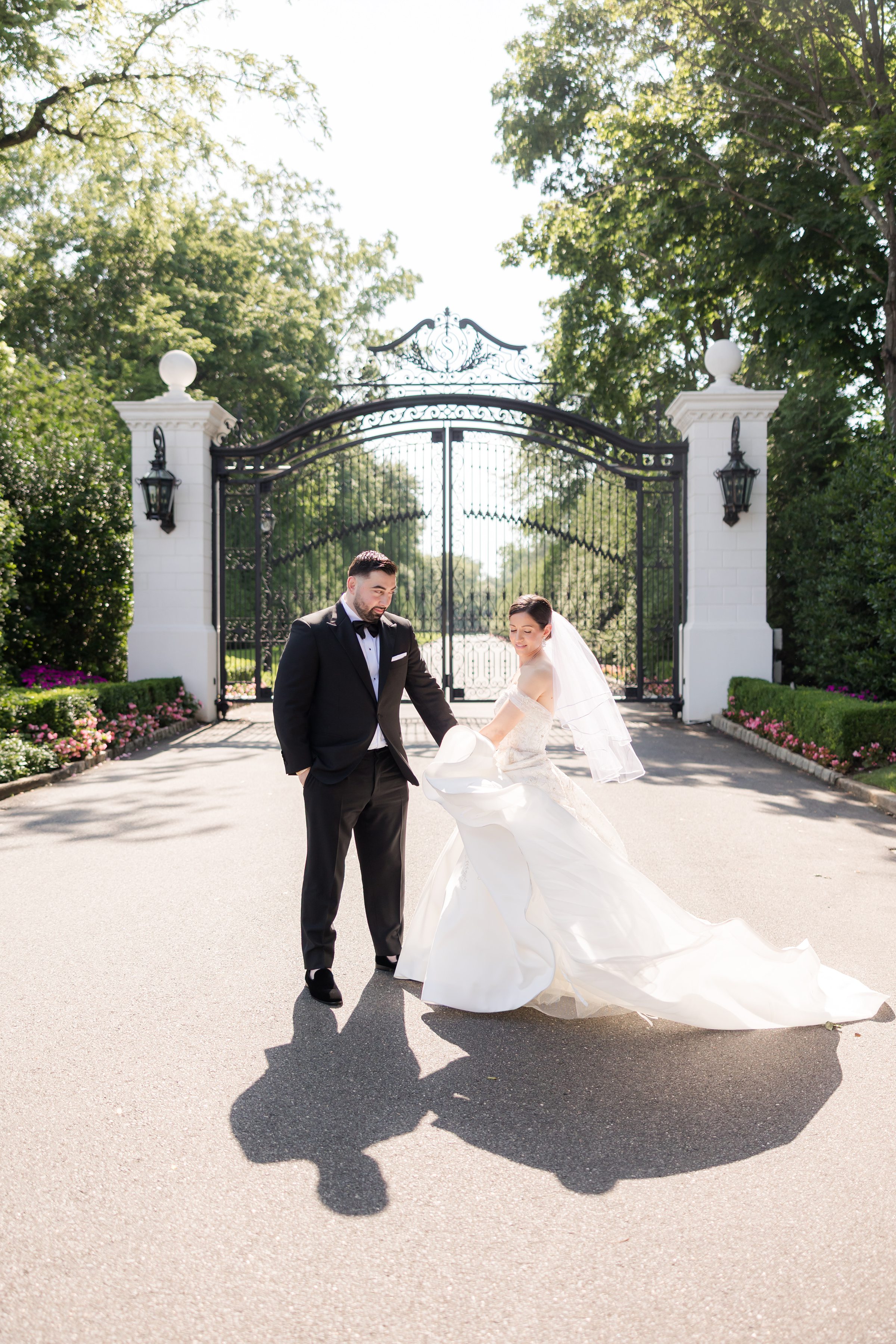 Bride and groom at the gates of Shadowbrook. Groom is looking at the bride while she twirls her dress, under the sunlight