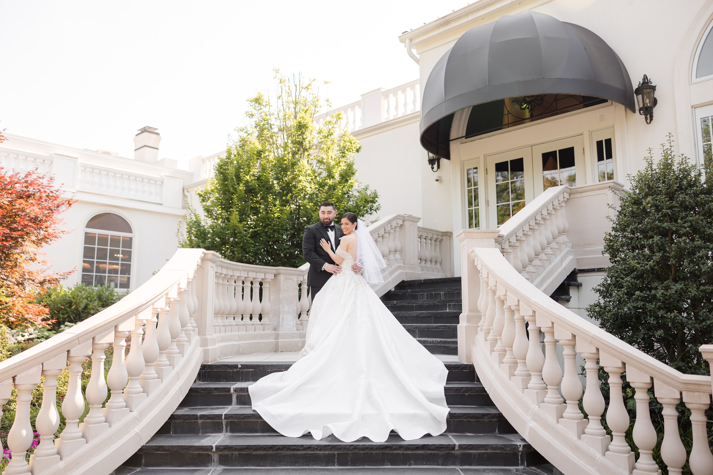 Landscape photo of bride and groom holding each other by the black stairs with white railings