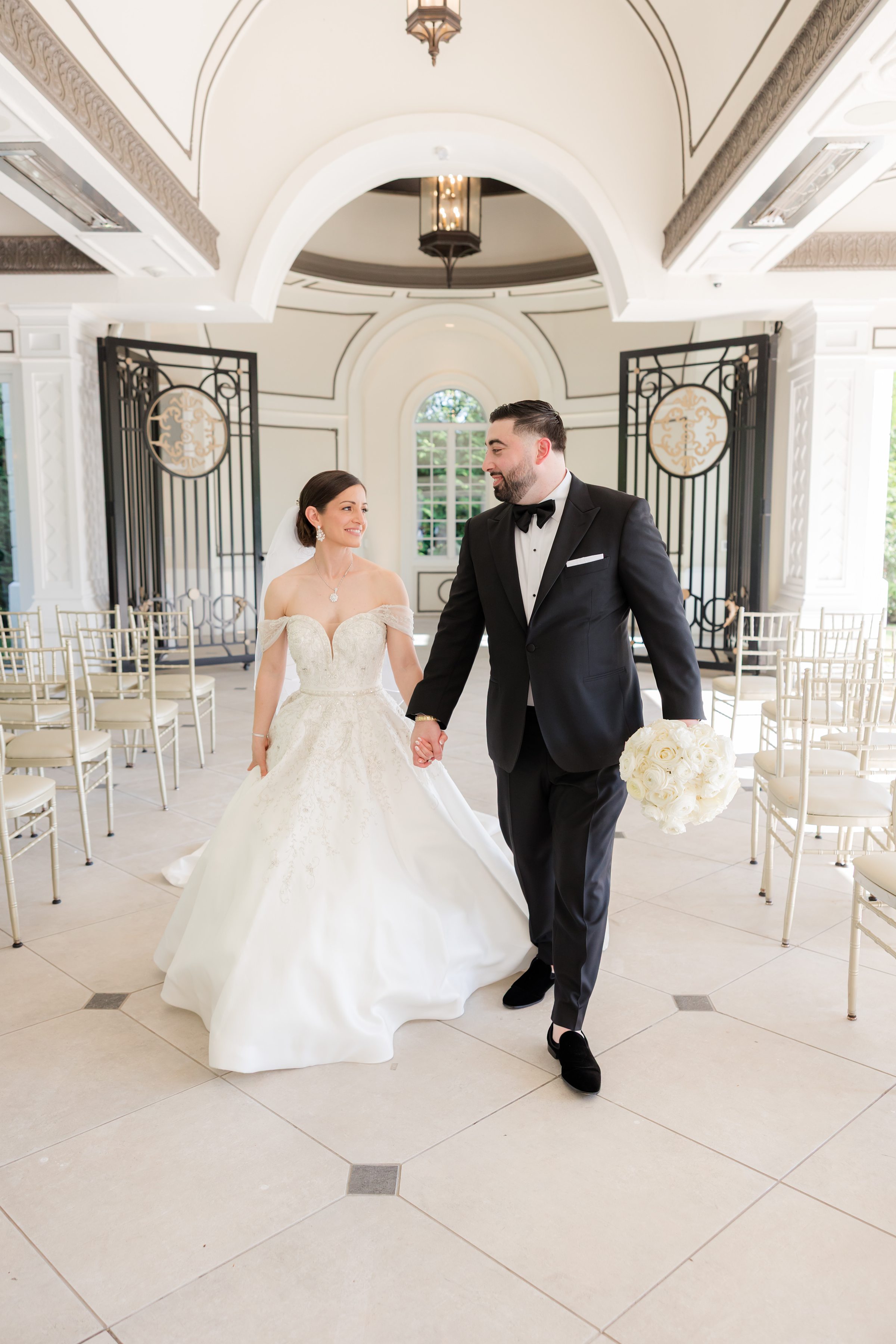 Photo of bride and groom walking inside Shadowbrook's chapel, groom is holding the bride's bouquet while they look at each other