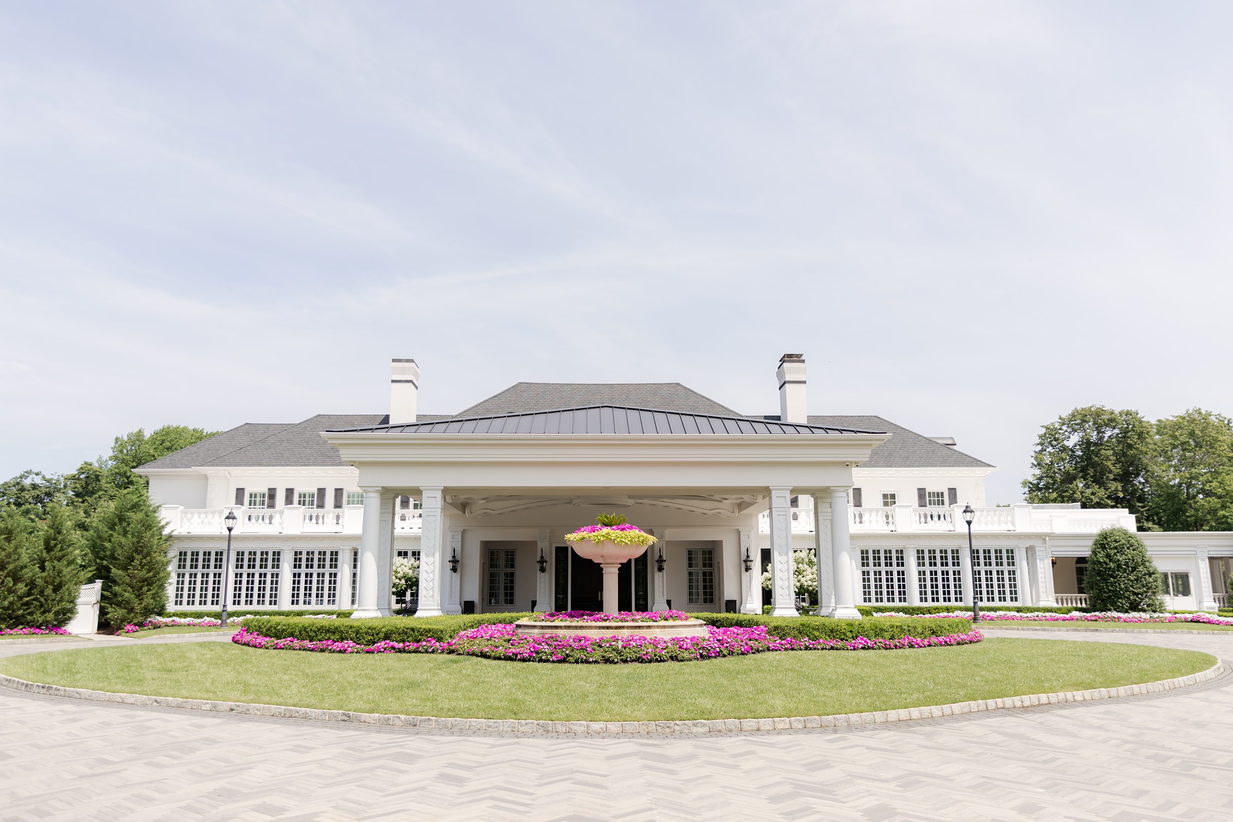 Shadowbrook's entrance. A 2-storey white building with gray roofing, 4 big columns in the entryway and a nice circular garden in front with pink flowers