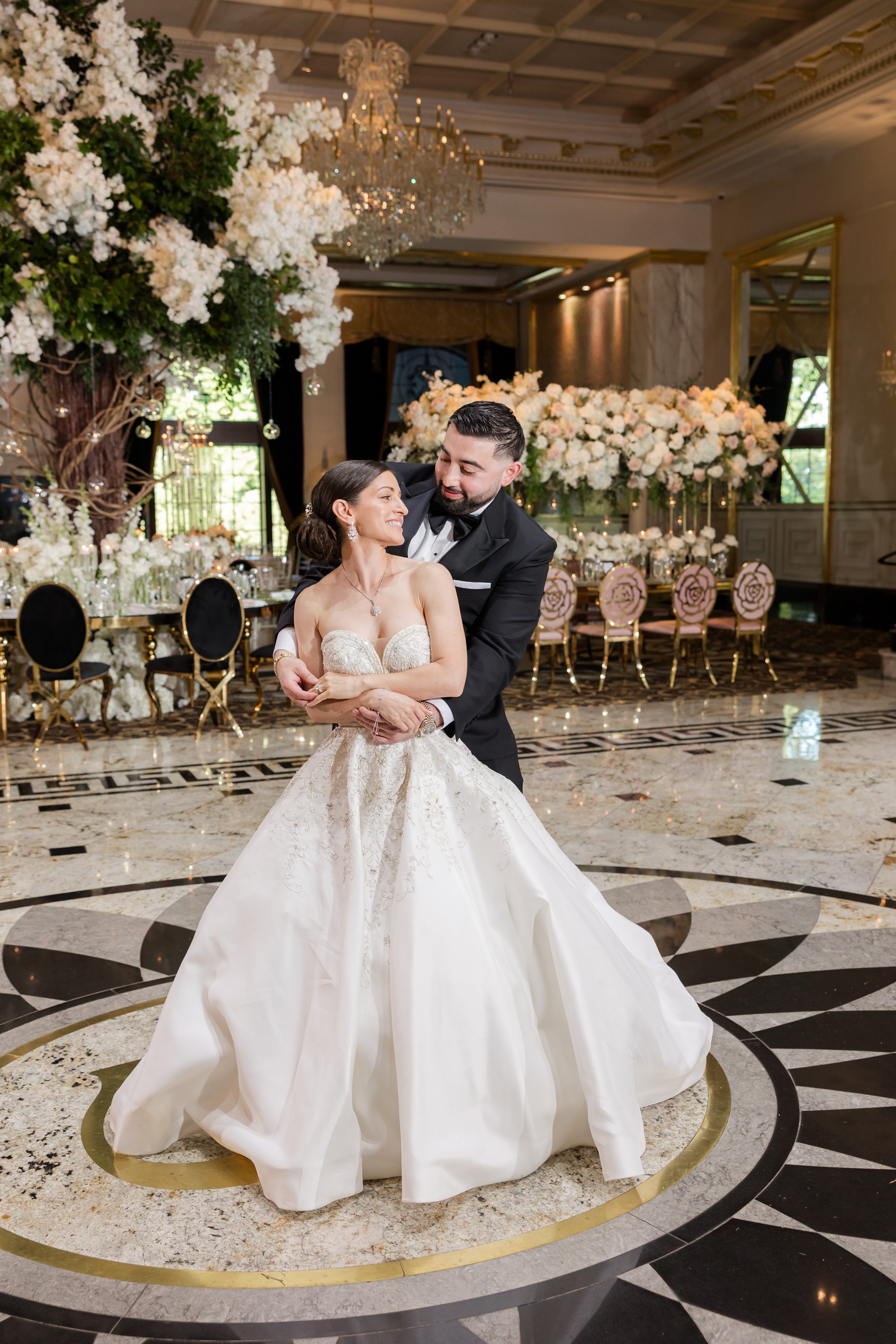 Photo of groom hugging the bride from behind, as they look into each other's eyes on an empty ballroom