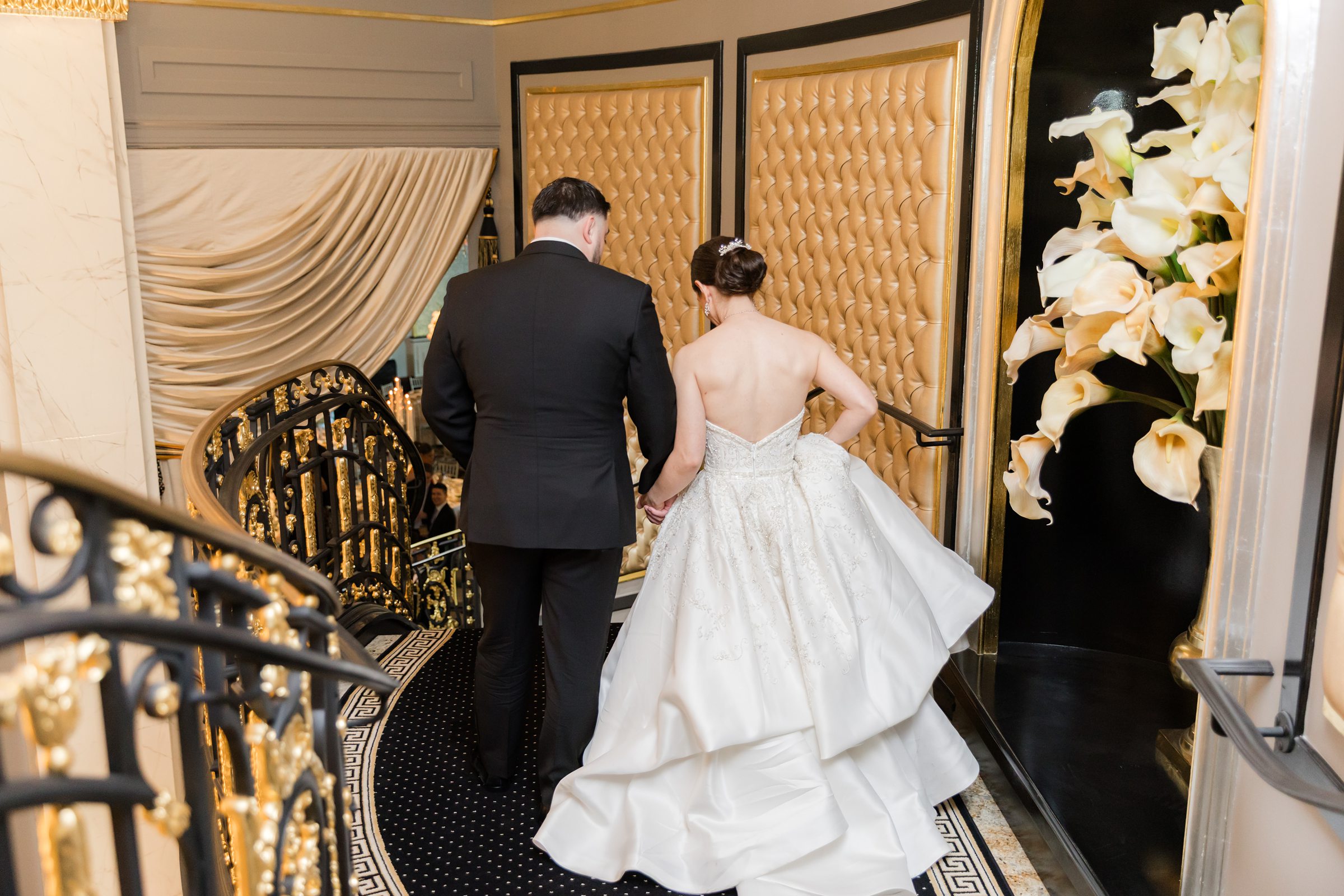 Bride and groom going down the staircase to enter the ballroom. The stairway is decorated with black and gold carpet with black and gold railings