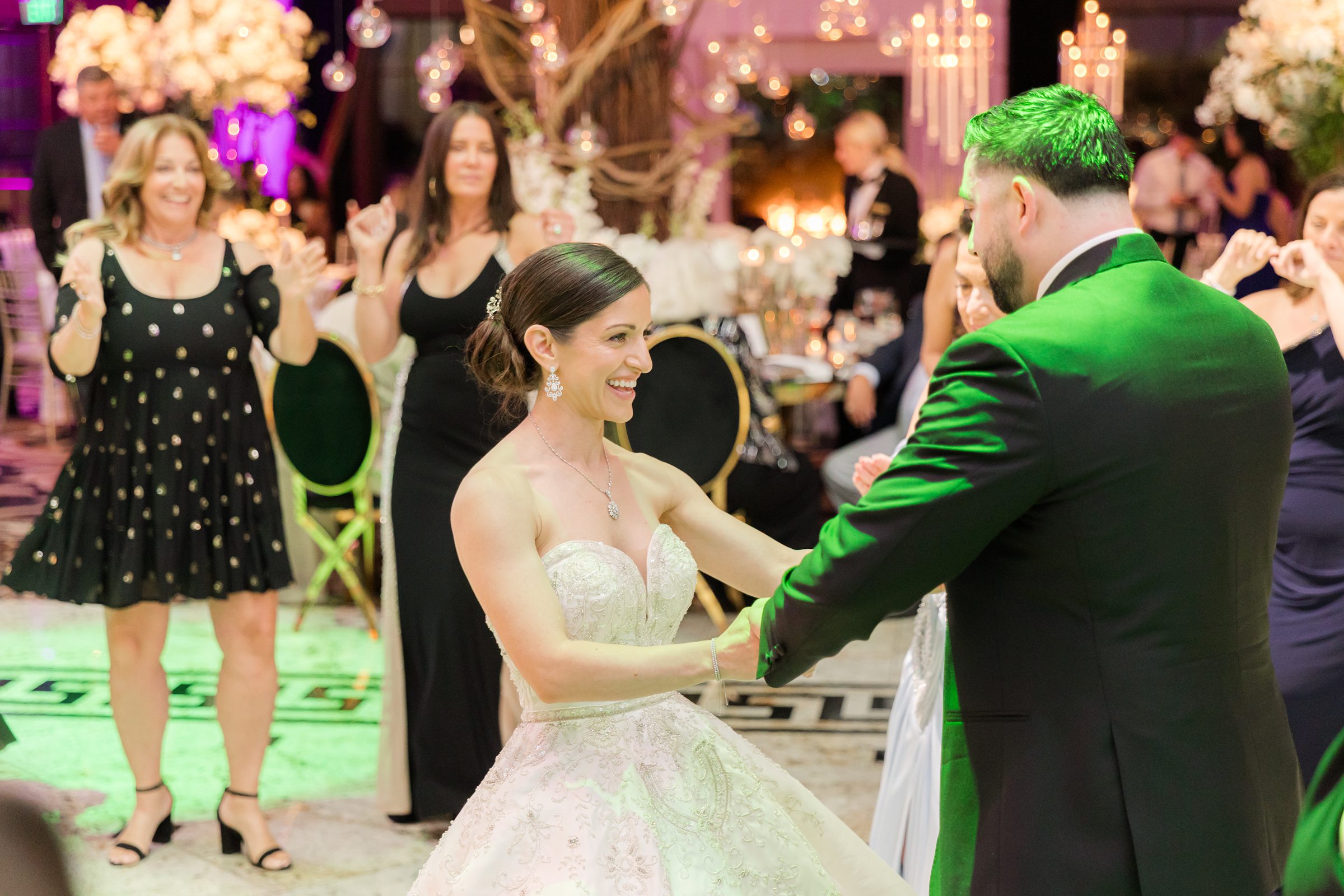 Photo of bride and groom dancing while guests are around them and pink lights are on