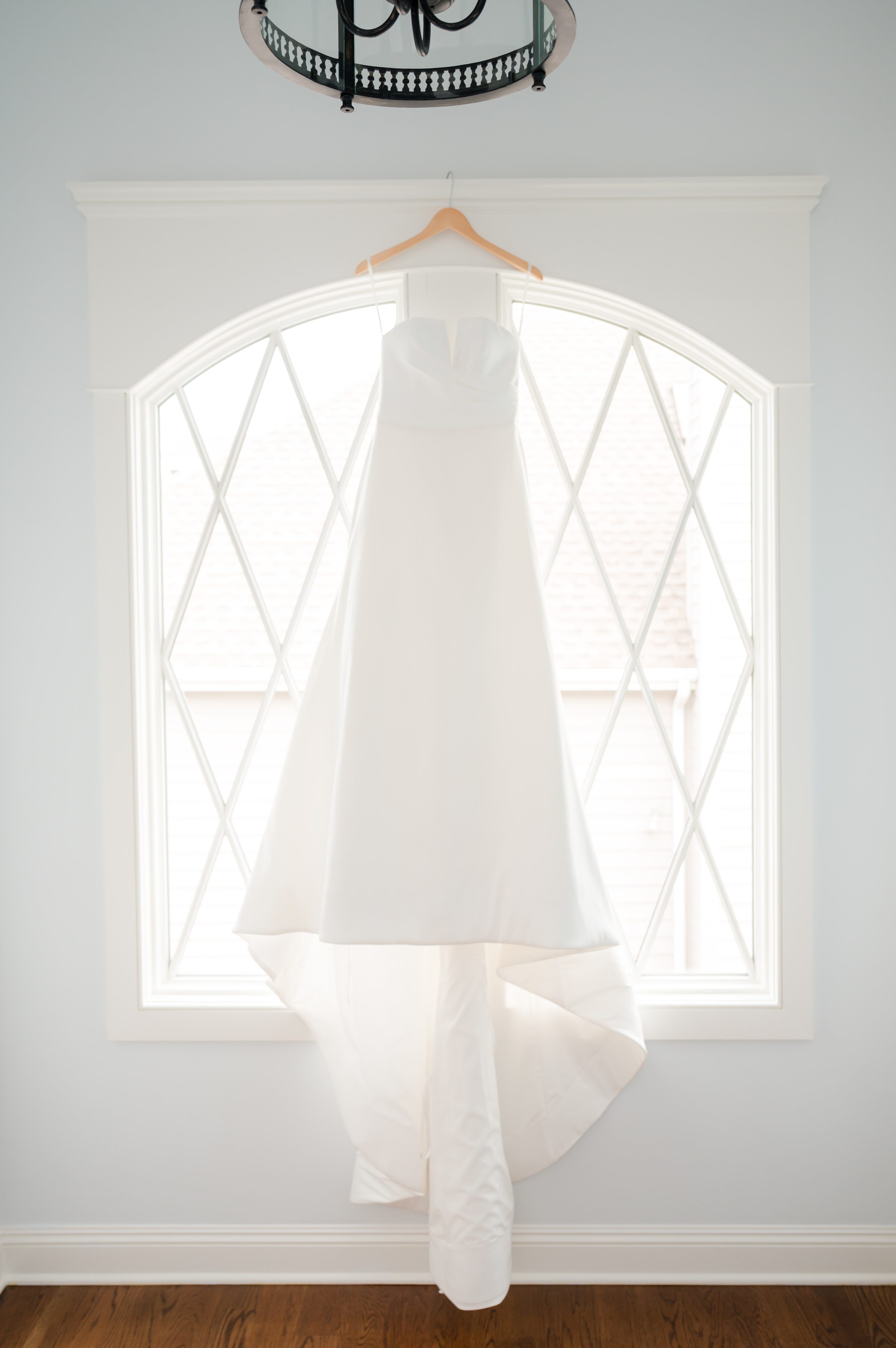 Wedding gown hangs in soft light by the window, waiting patiently for the moment it becomes part of a lifelong memory