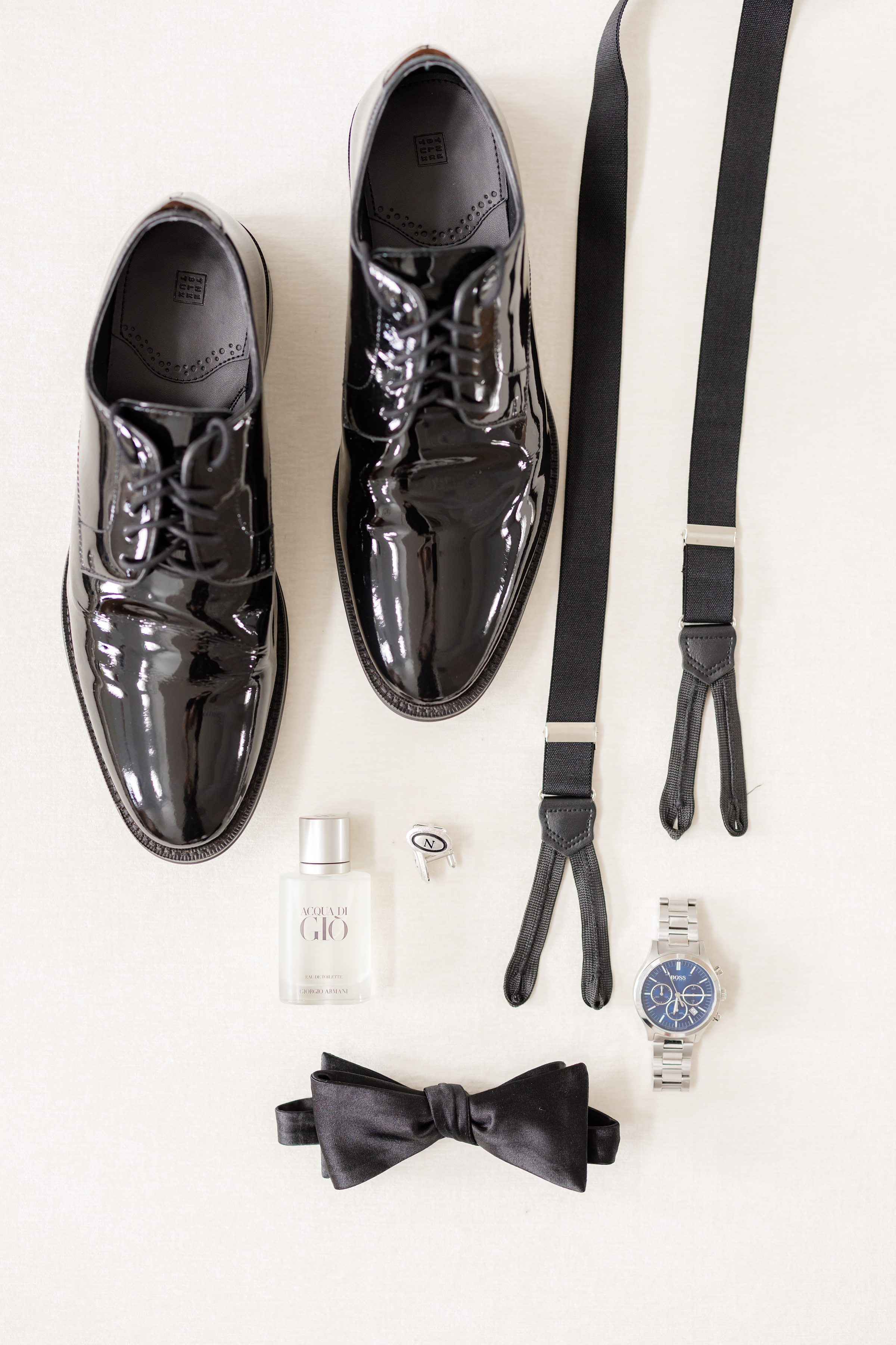 Elegant groom accessories—polished black shoes, silk bow tie, and timeless details—carefully arranged in anticipation of a wedding day filled with love.