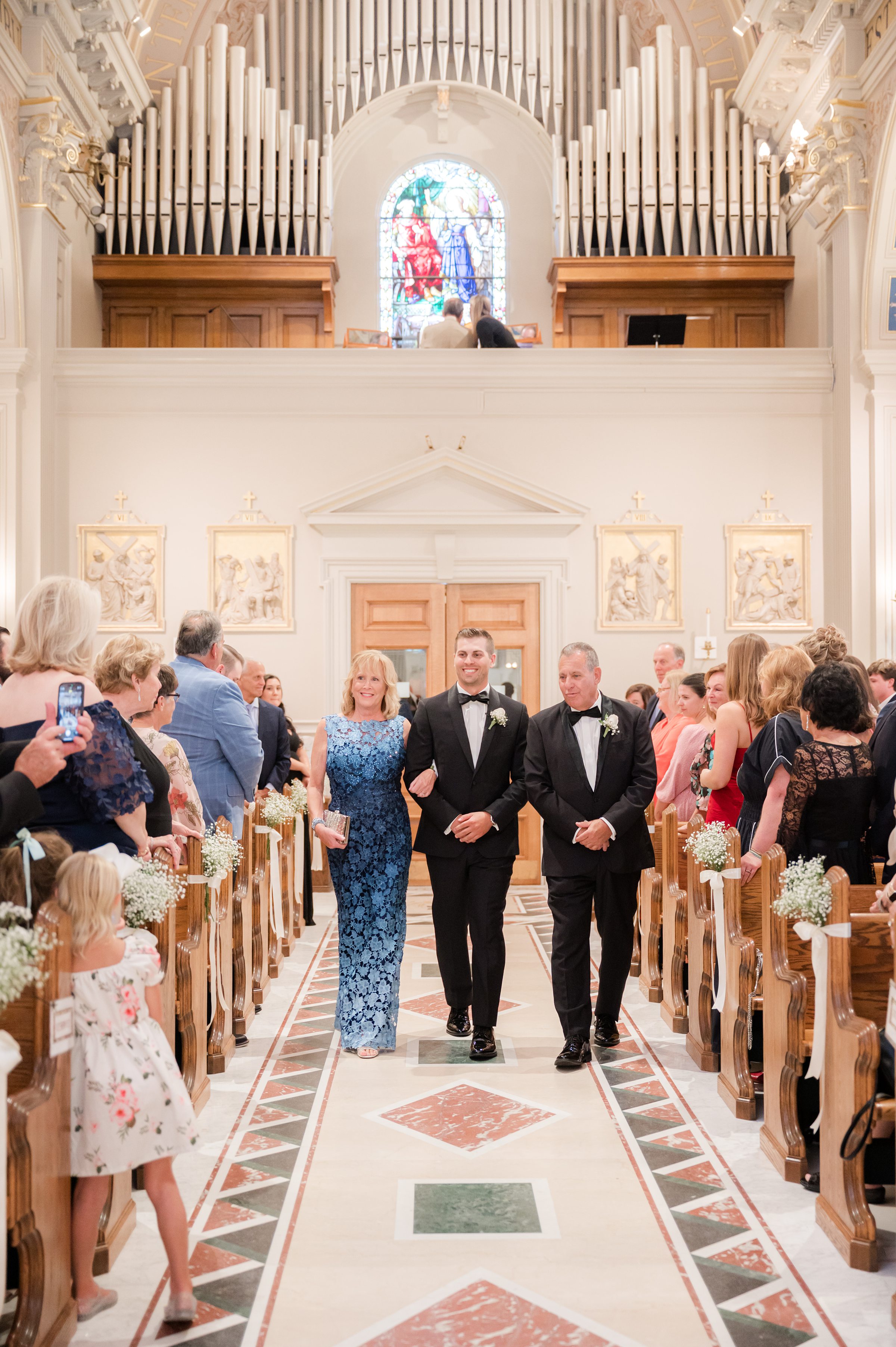 Groom walks down the aisle with his parents, surrounded by loved ones, as he makes his way toward the start of a new chapter