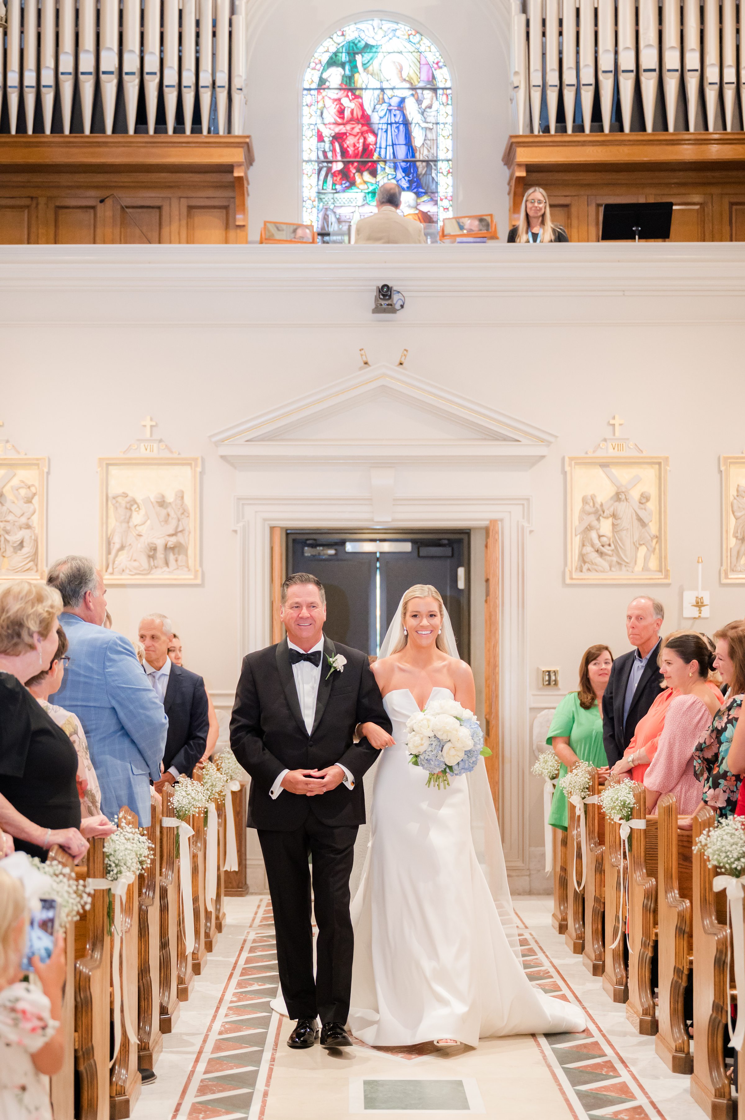 Bride walks down the aisle with her father, carrying both love and anticipation toward the one waiting for her.”