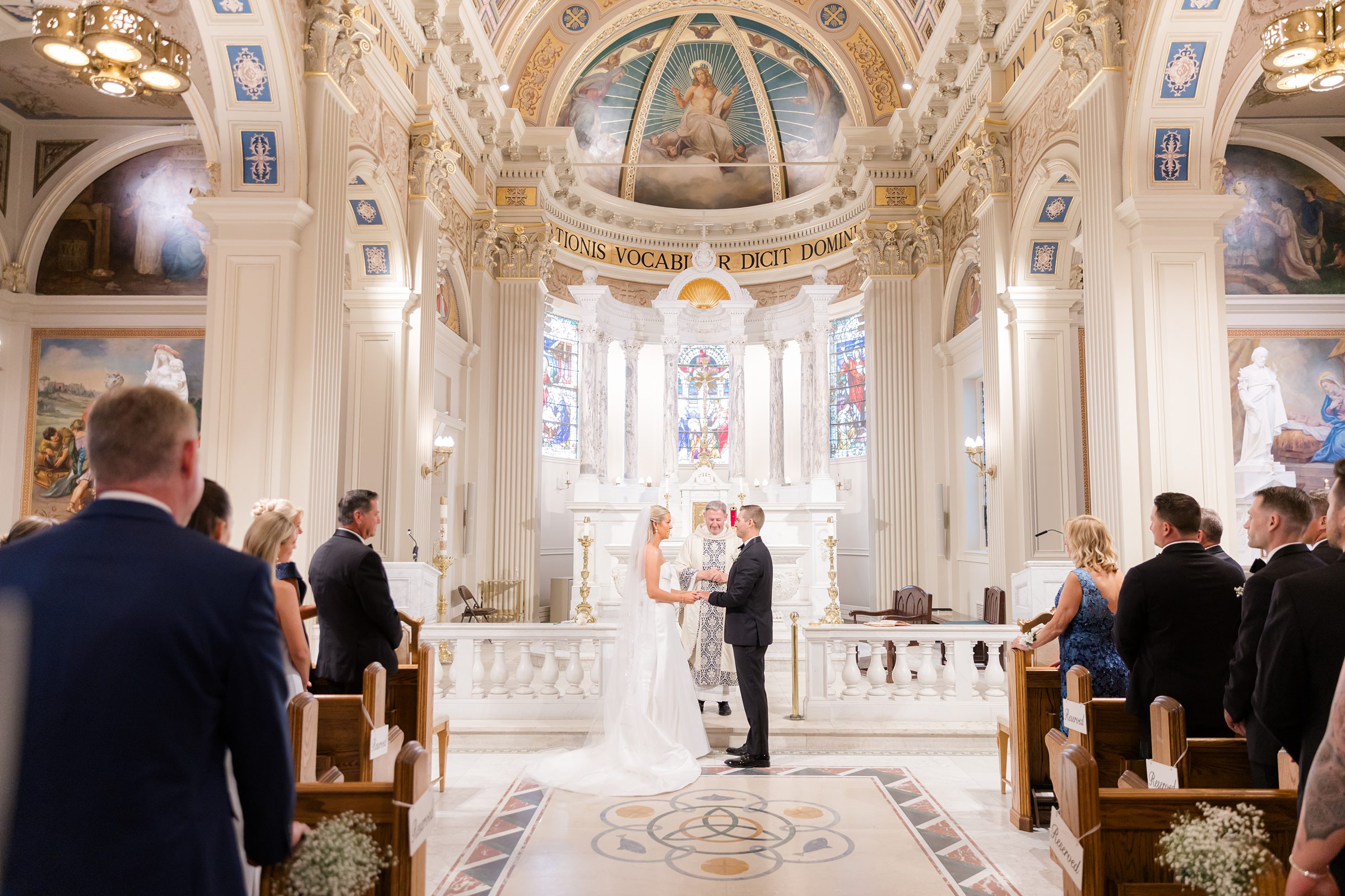 Bride and groom stand together at the altar, exchanging vows beneath the grand, light-filled beauty of the church