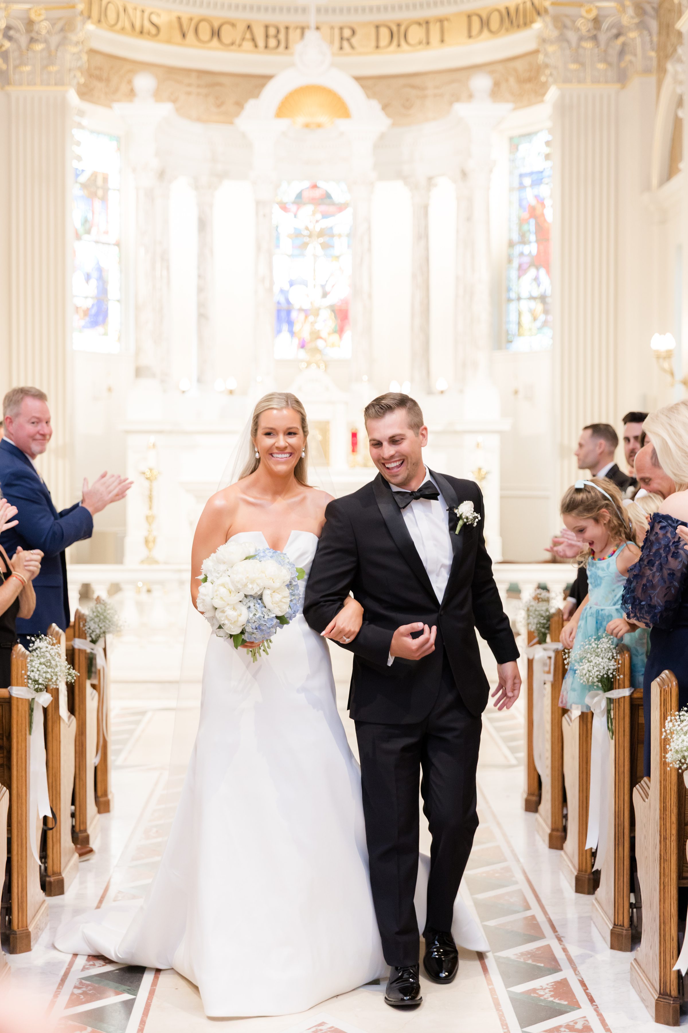 Radiant with joy, the newlyweds walk together down the aisle, greeted by smiles and applause from those who love them most