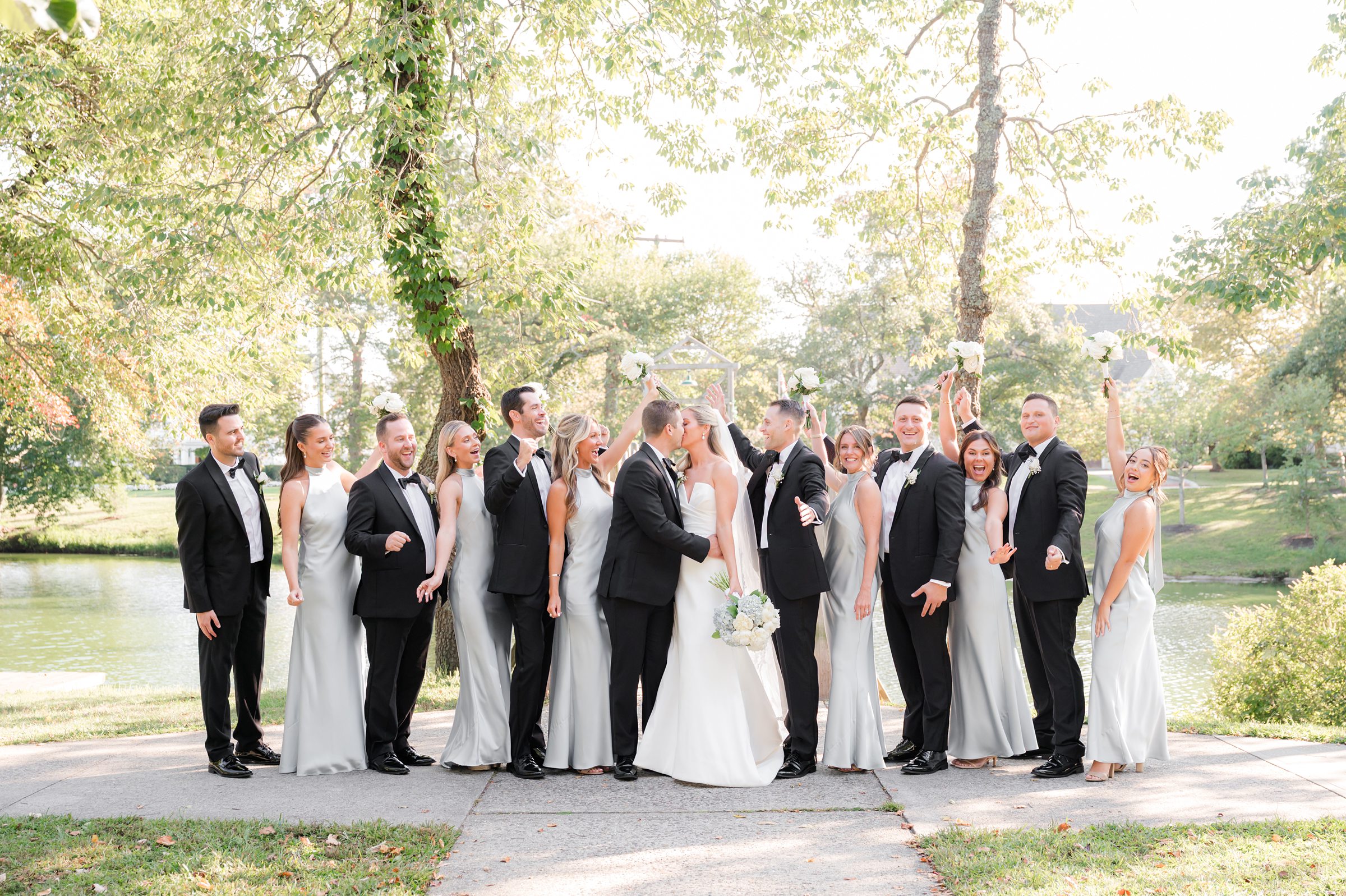 Joyful wedding party surrounds the couple as they share a kiss, capturing pure celebration and love.