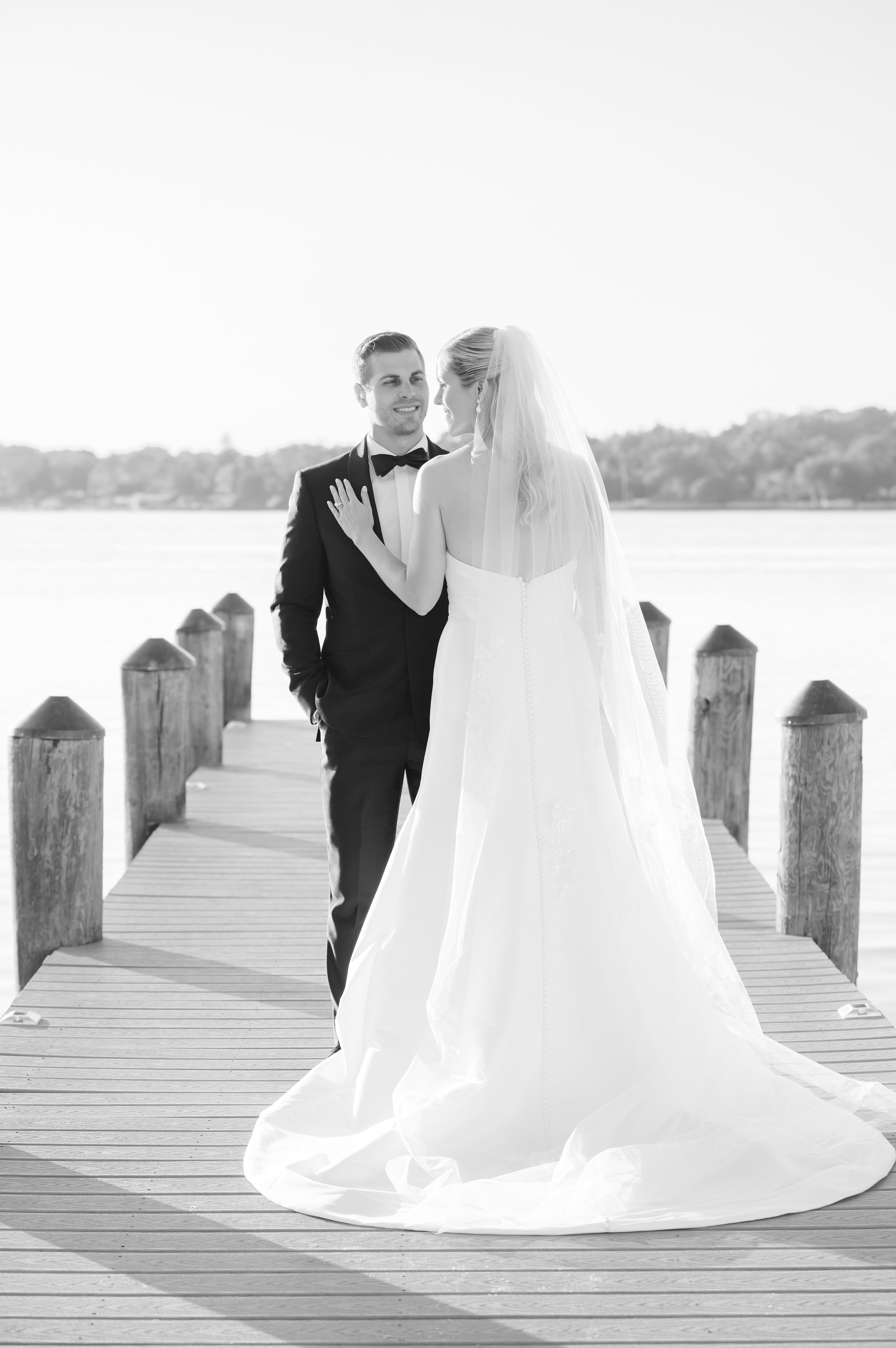 Bride and groom share a quiet, intimate moment on a wooden dock, the bride gently resting her hand on his chest as they gaze at each other with soft smiles