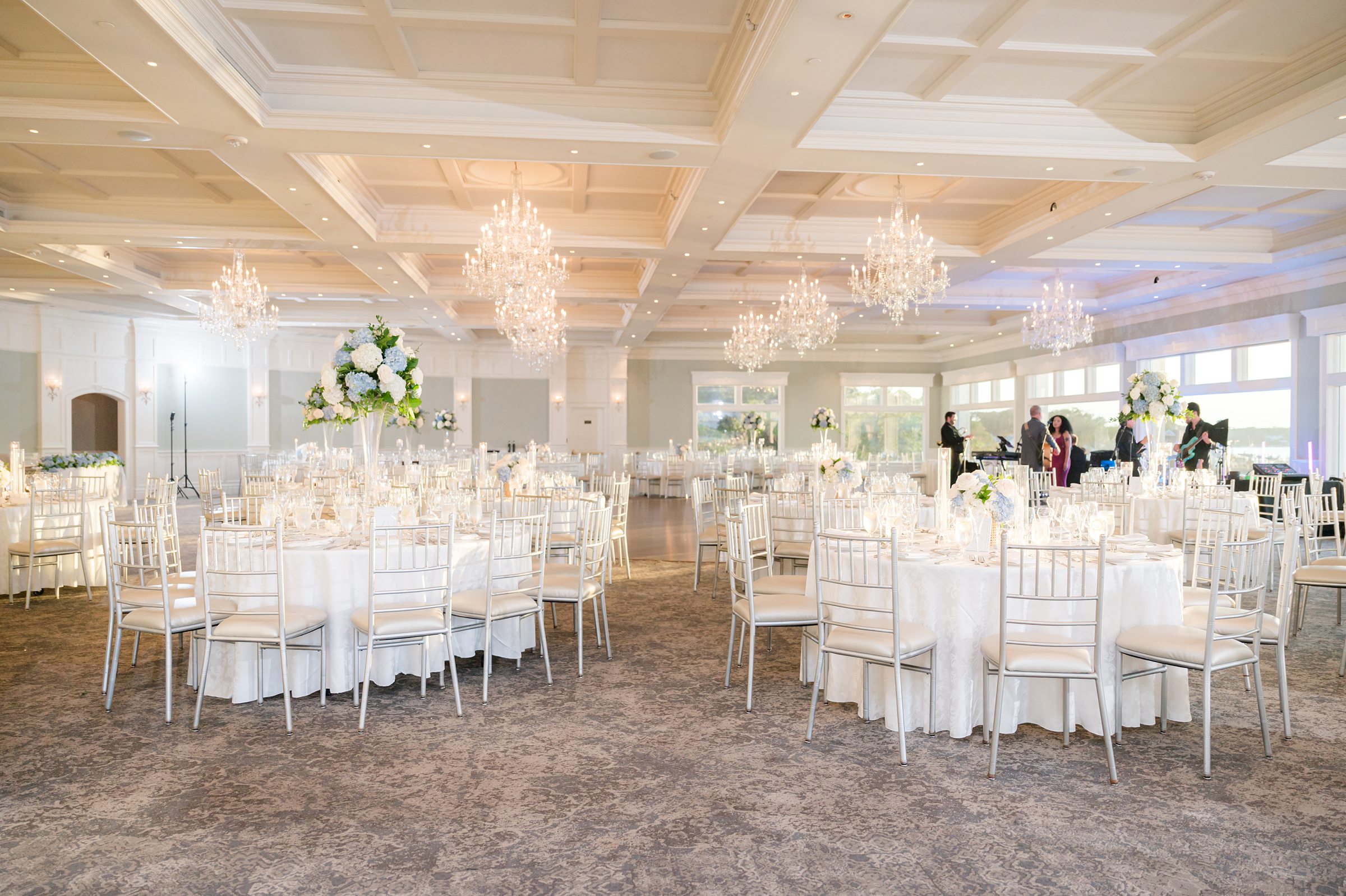 Luminous wedding reception space adorned with crystal chandeliers and soft florals awaits a night of love and celebration.