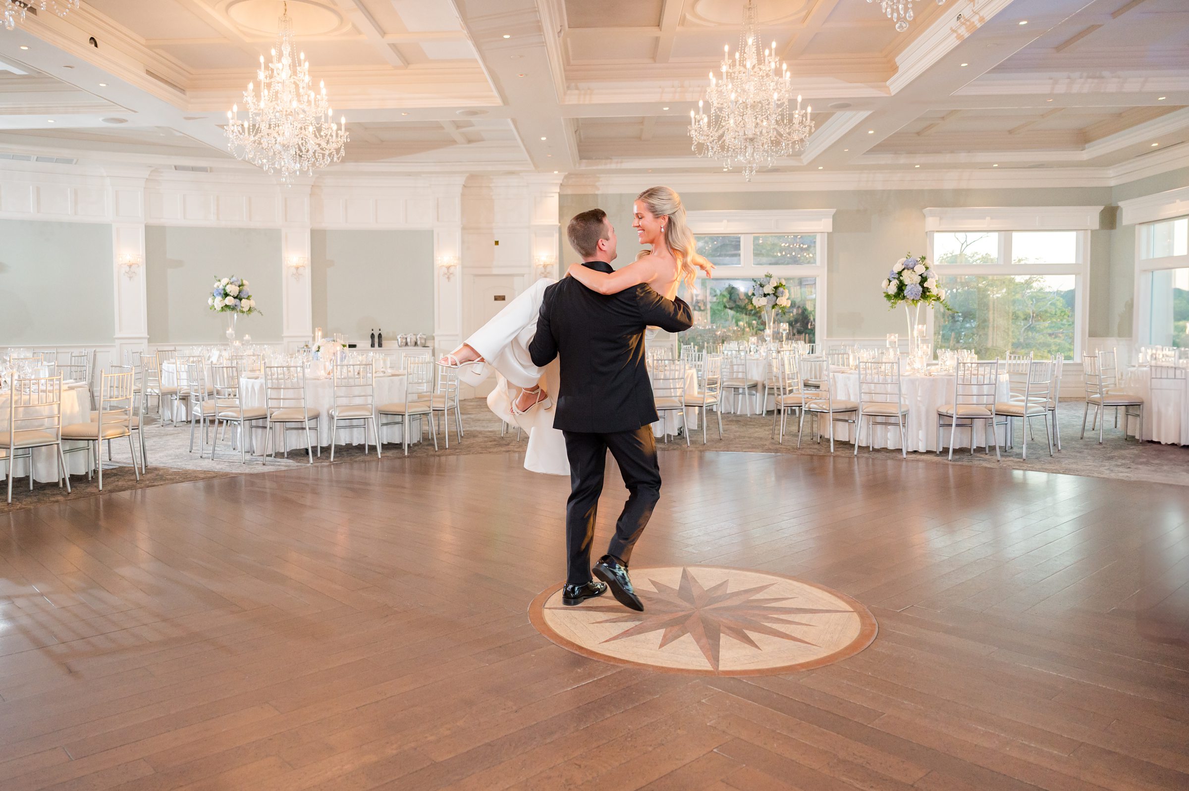 Newlyweds share a joyful, intimate moment as the groom lifts his bride beneath glowing chandeliers in an elegant reception hall