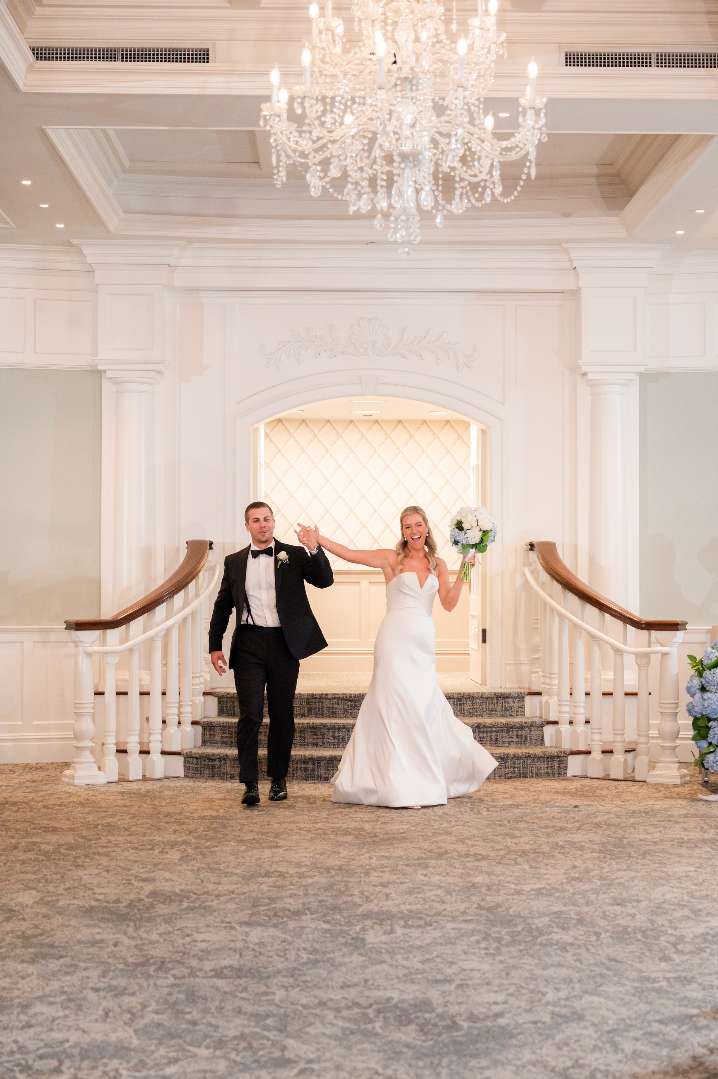 Bride lifts her bouquet with excitement while the groom walks beside her, both glowing with happiness and love.
