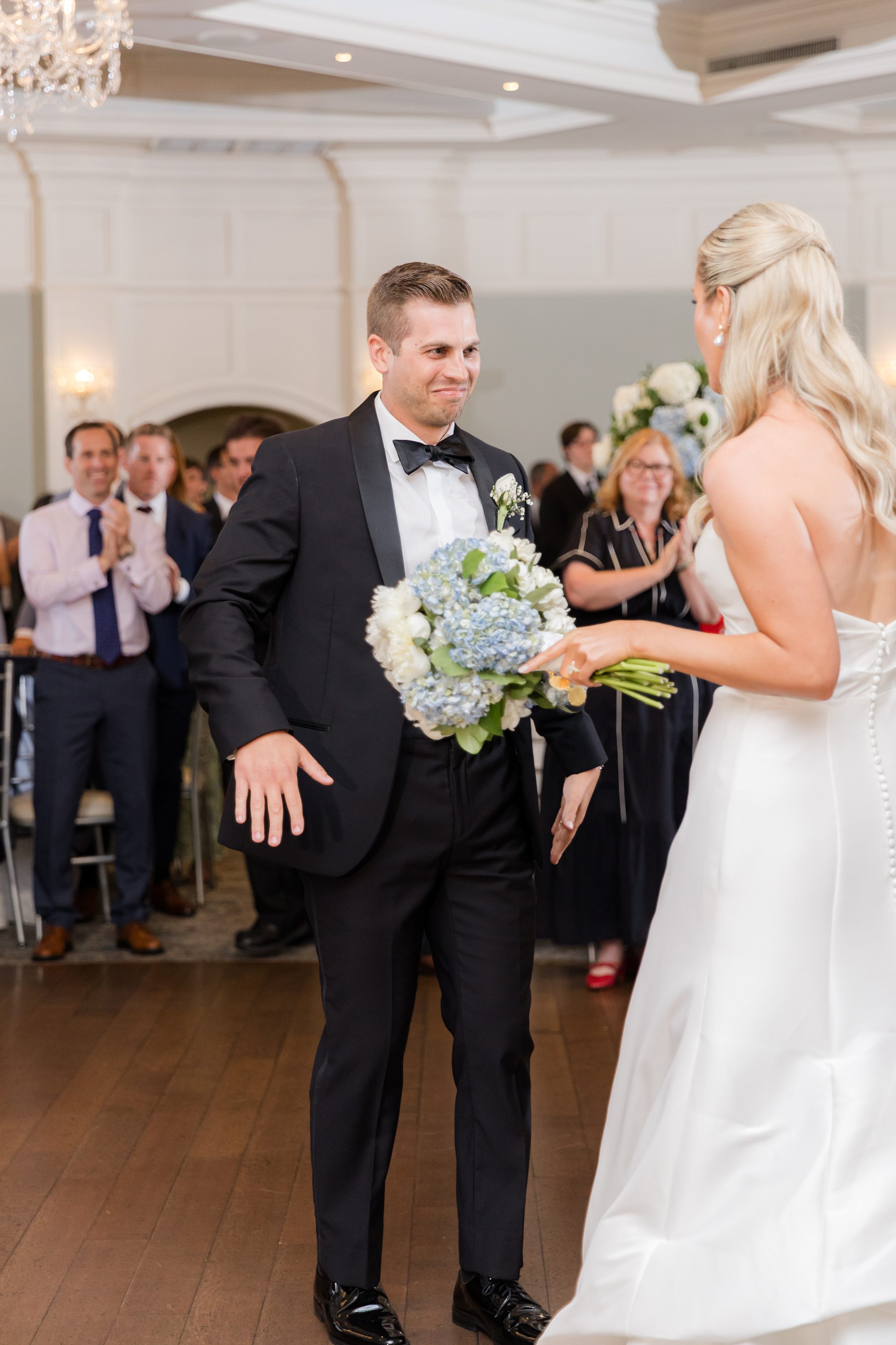 Groom smiles warmly at the bride as she holds her bouquet, sharing a joyful moment during their celebration