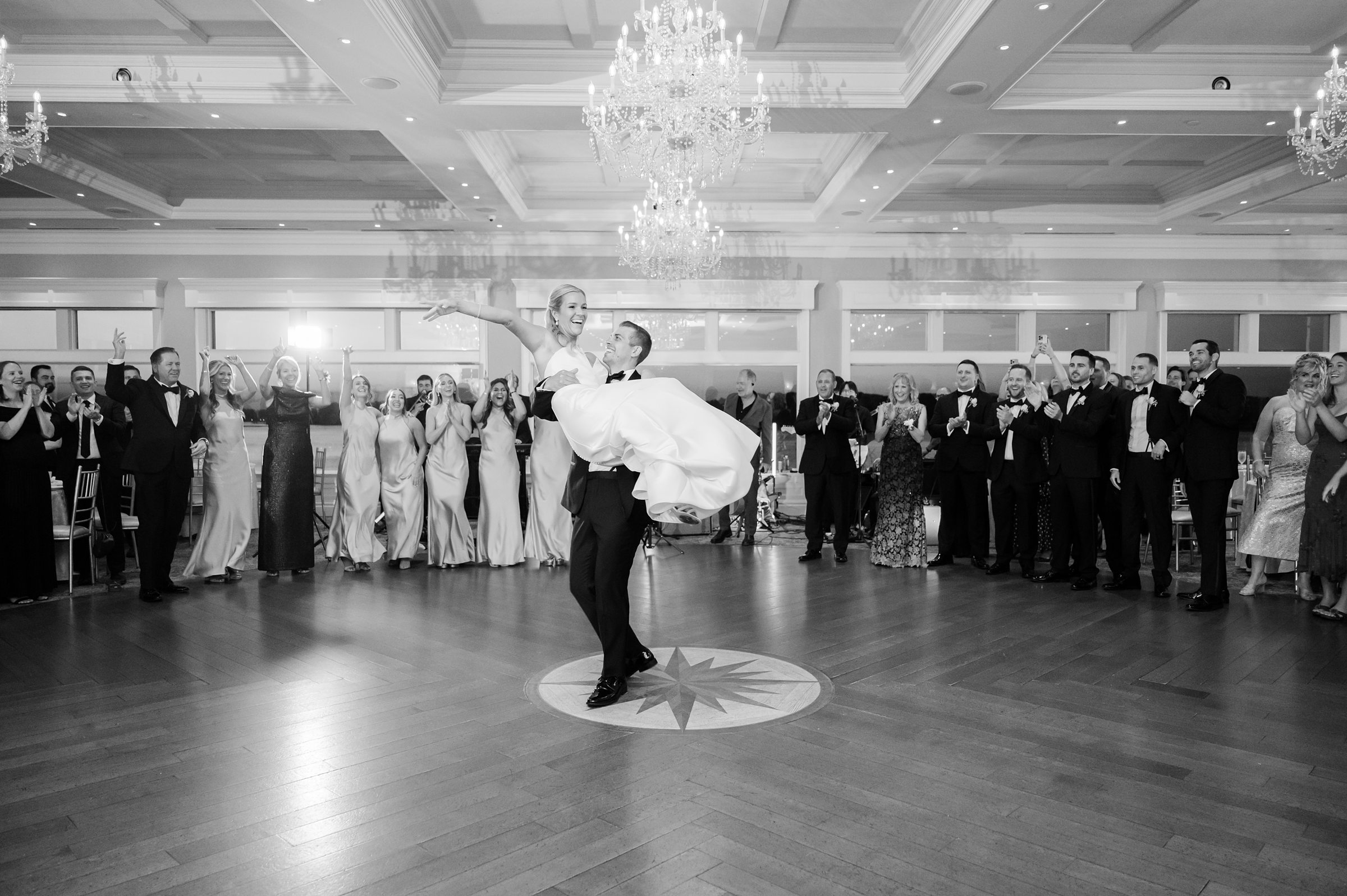 Groom lifts the bride effortlessly in the center of the dance floor as guests surround them, celebrating their love.