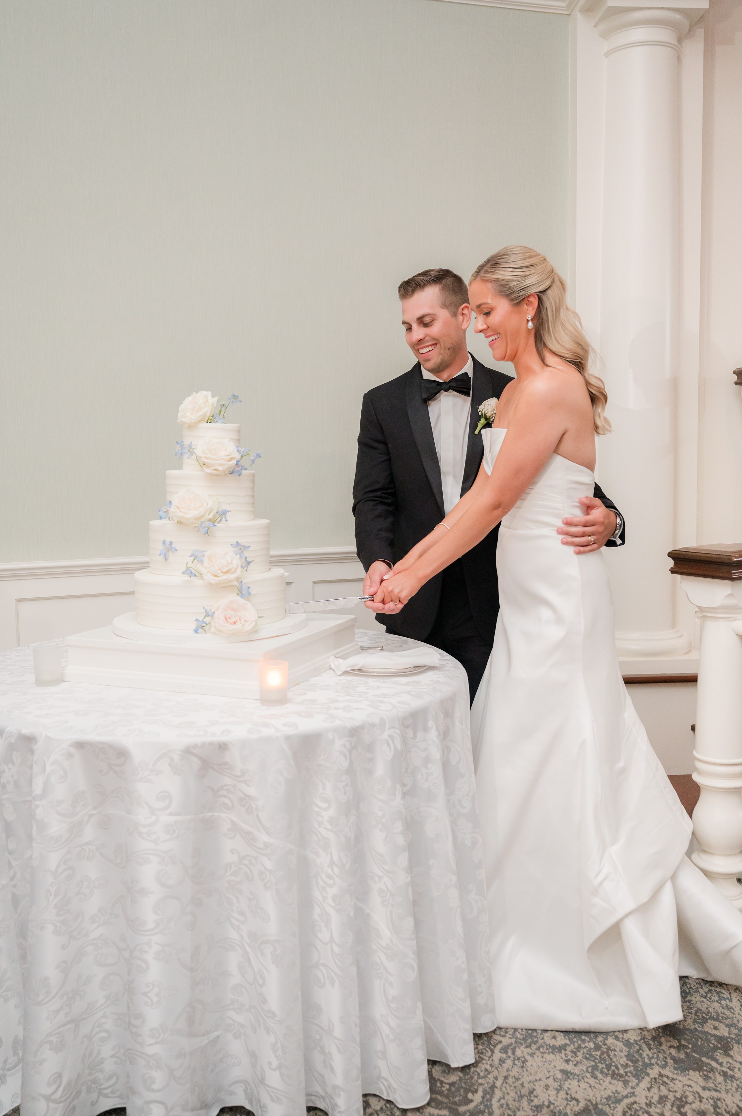 Bride and groom stand close together as they cut their wedding cake, his arm wrapped gently around her in a loving embrace.