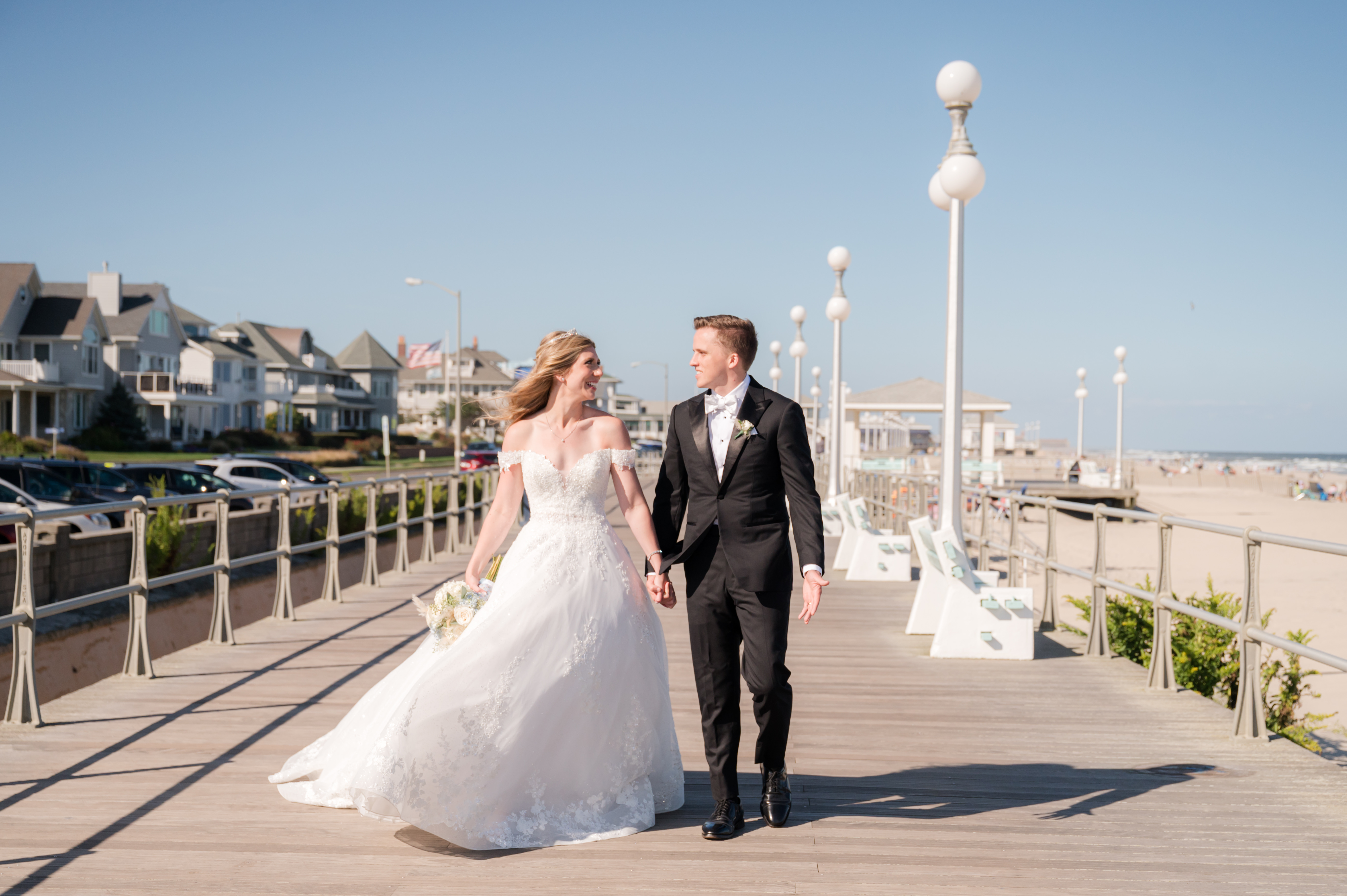 Bride and groom walking by the beach while looking at each other and holding hands